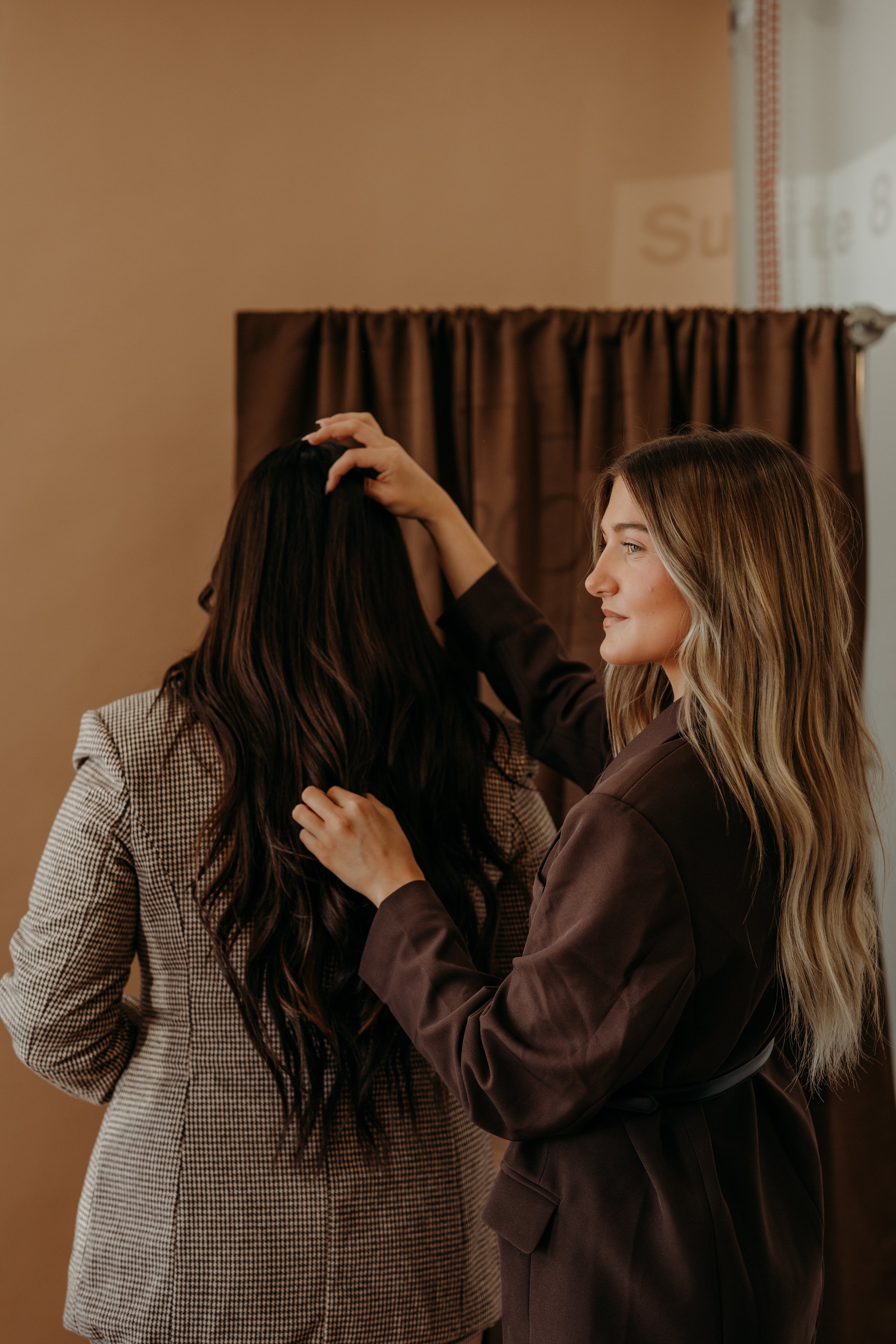Raegan Becker styling a client's long, wavy brunette invisible bead extensions at Haus of Opal in Topeka, Kansas