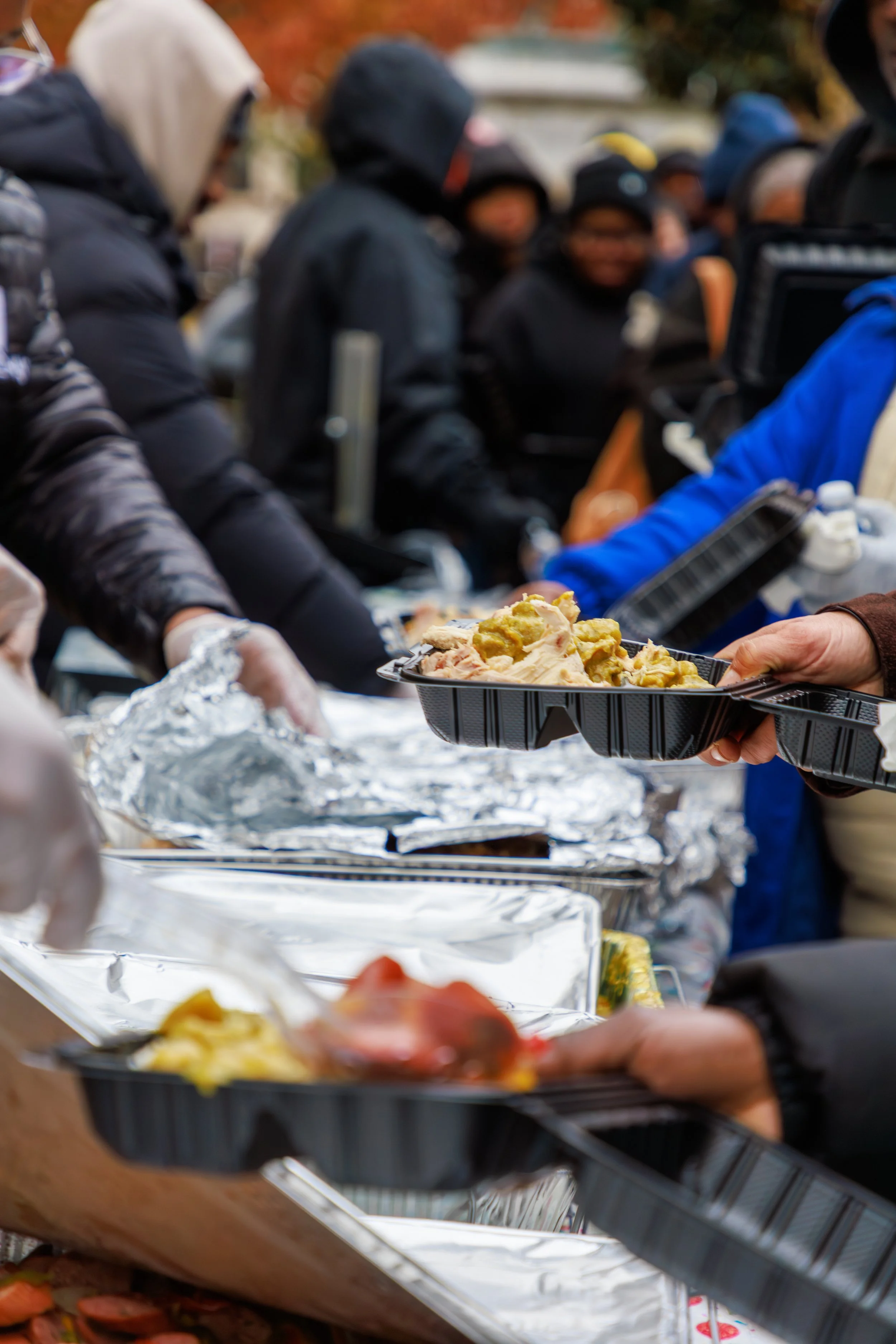 People in warm clothing serving food from trays at an outdoor event during fall.