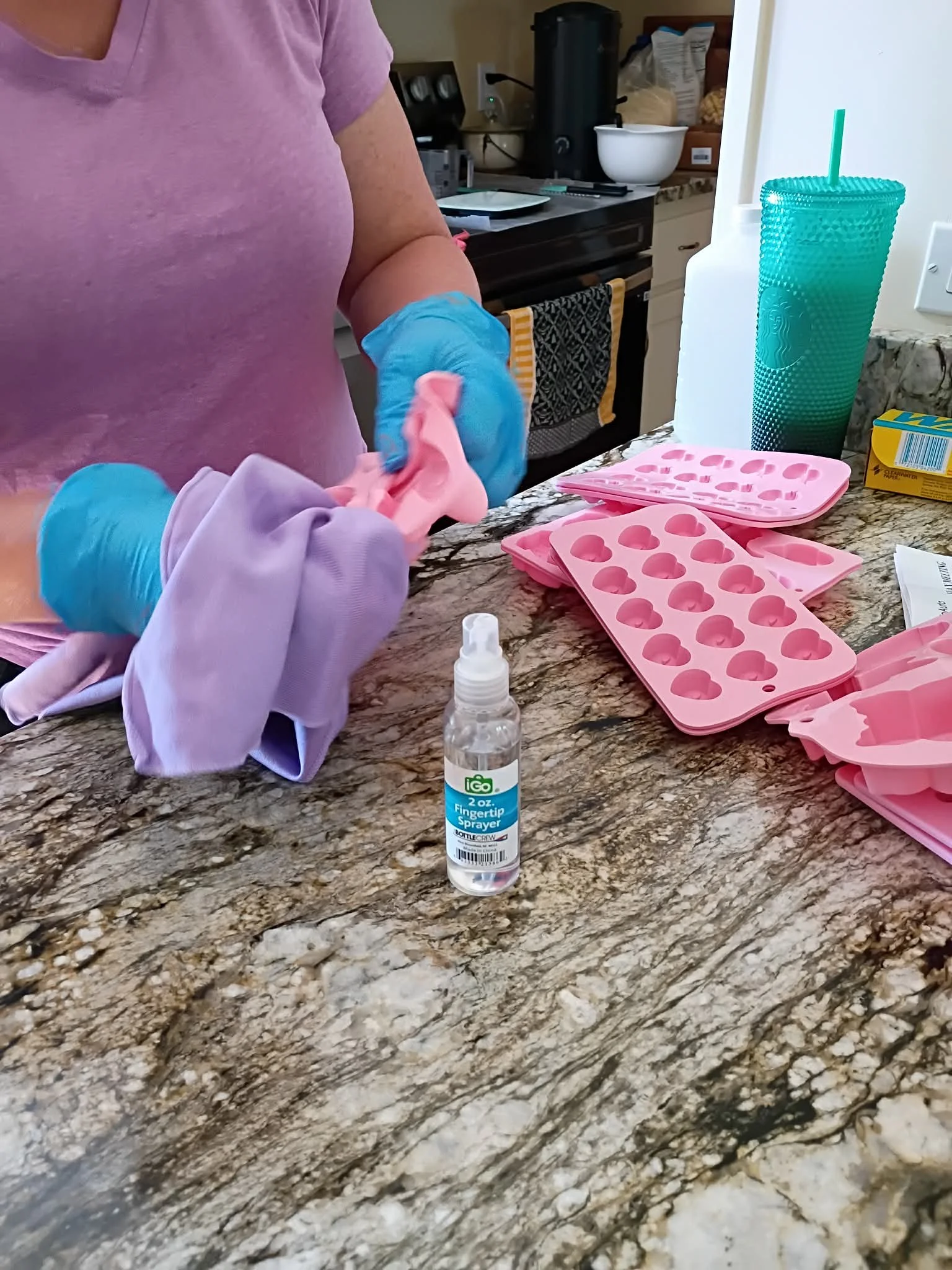 Person wearing purple shirt and blue gloves preparing pink silicone ice cube molds on a kitchen countertop.