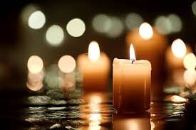 Two lit candles reflecting on water with blurred lights in the background.