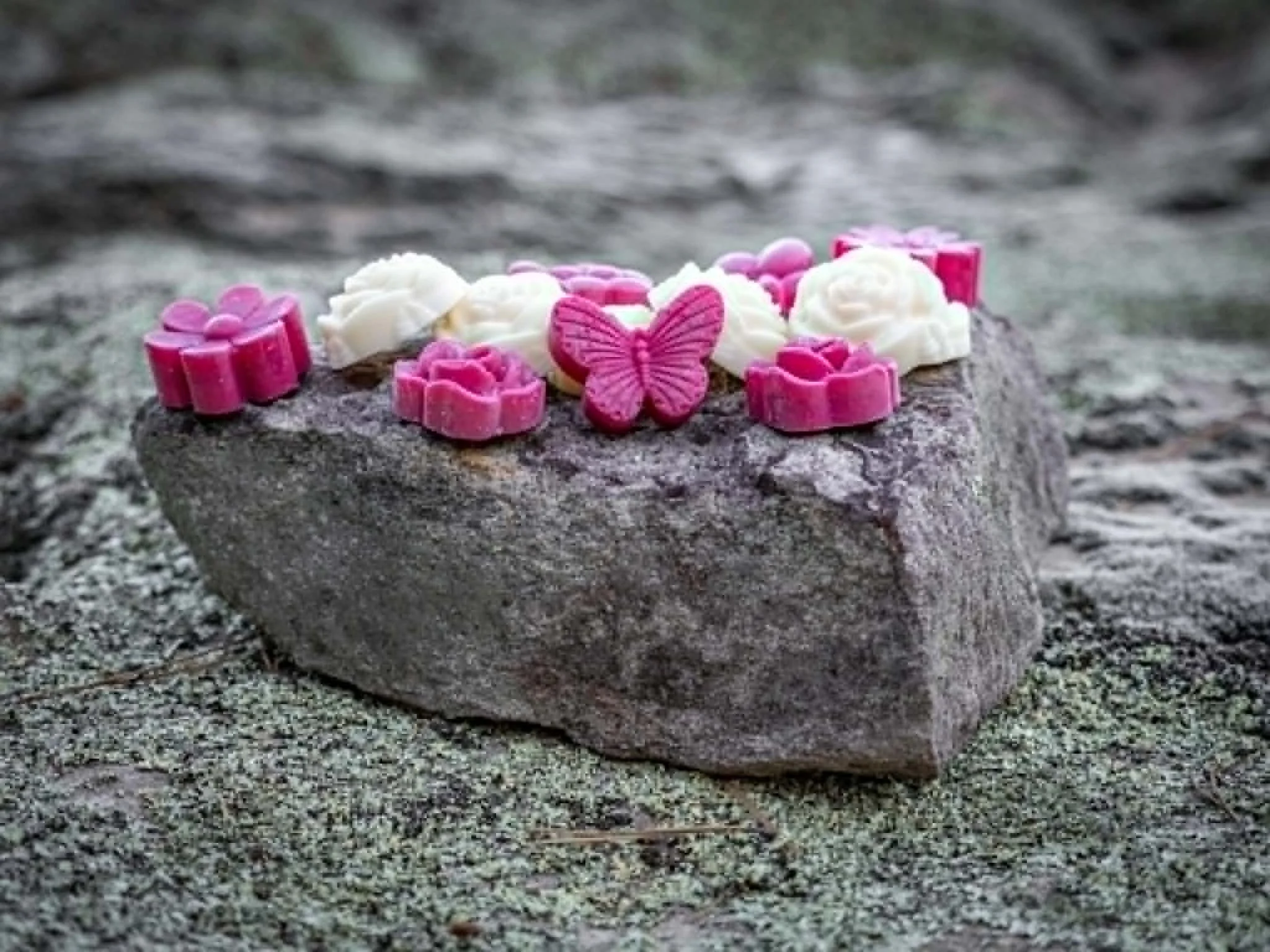 Pink and white flower-shaped candies and a pink butterfly-shaped candy are arranged on a rock.