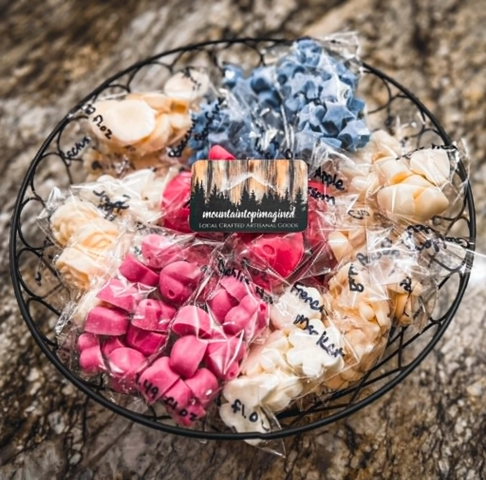 A wire basket filled with wrapped candies of various colors, including pink, white, and orange, on a granite countertop.