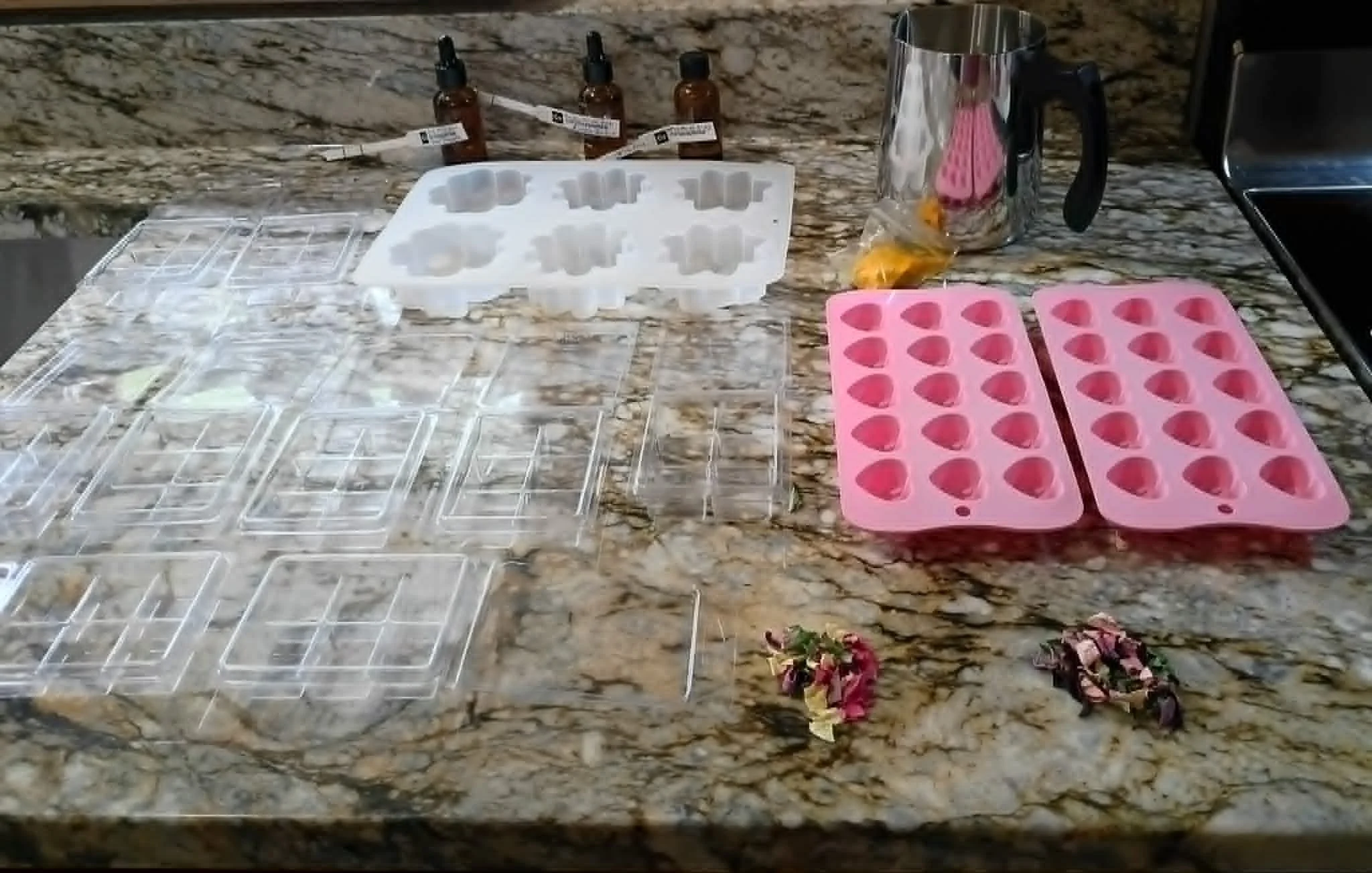 Assorted ice cube trays and ingredients for making soap or candles on a kitchen countertop.