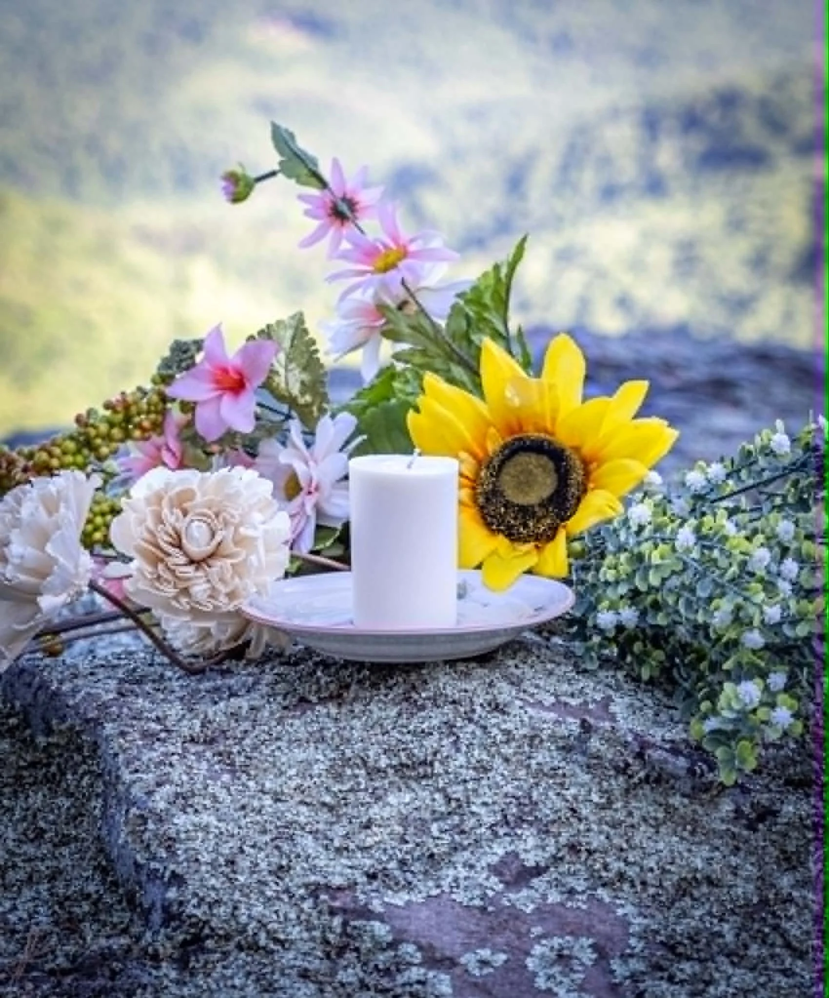 A floral arrangement with pink, white, and yellow flowers, including a sunflower, placed on a gravel surface outdoors.