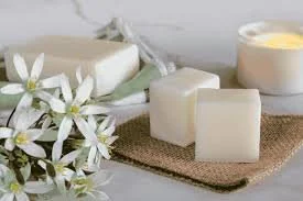 Soap bars, a bowl of lotion, and white flowers on a wooden mat