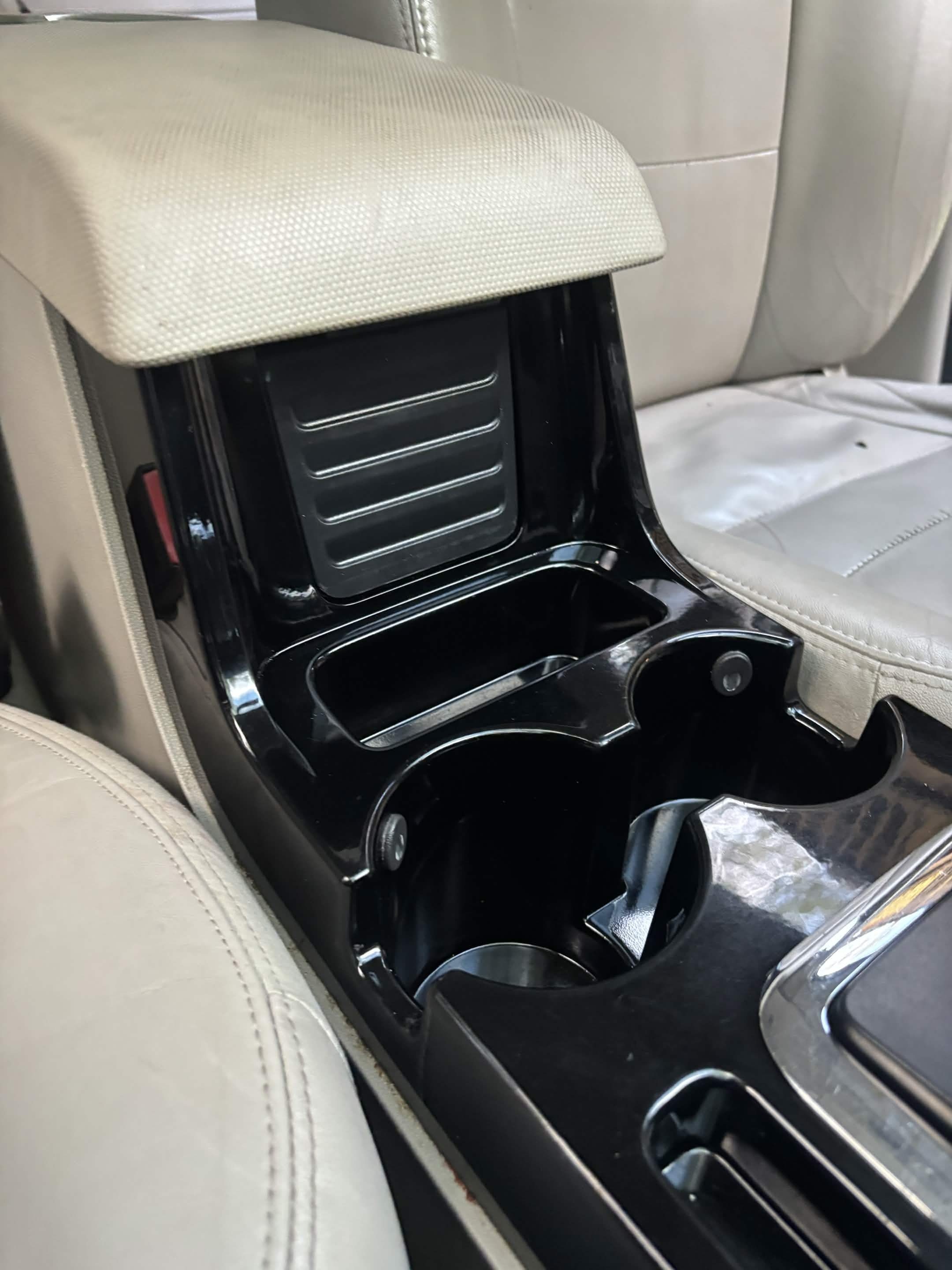 Car interior with beige leather seats, black center console, and cup holders.