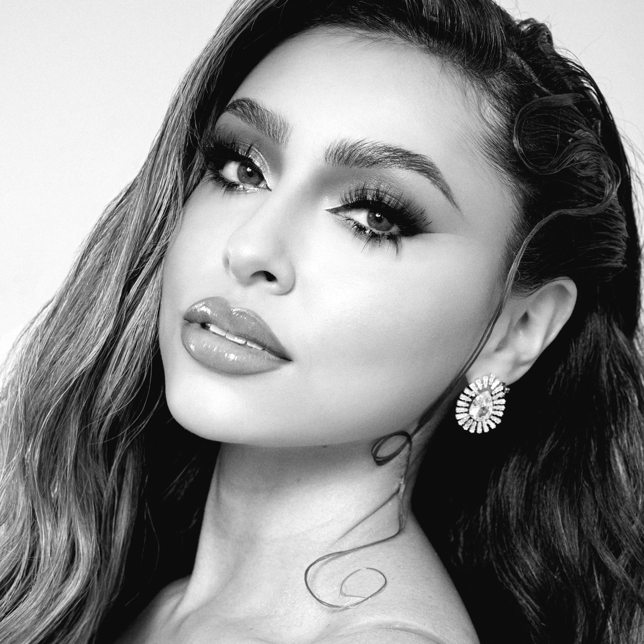 Close-up of a woman's face highlighting her eye makeup, eyebrows, and lips, with her hair sweeping across her face, in black and white.