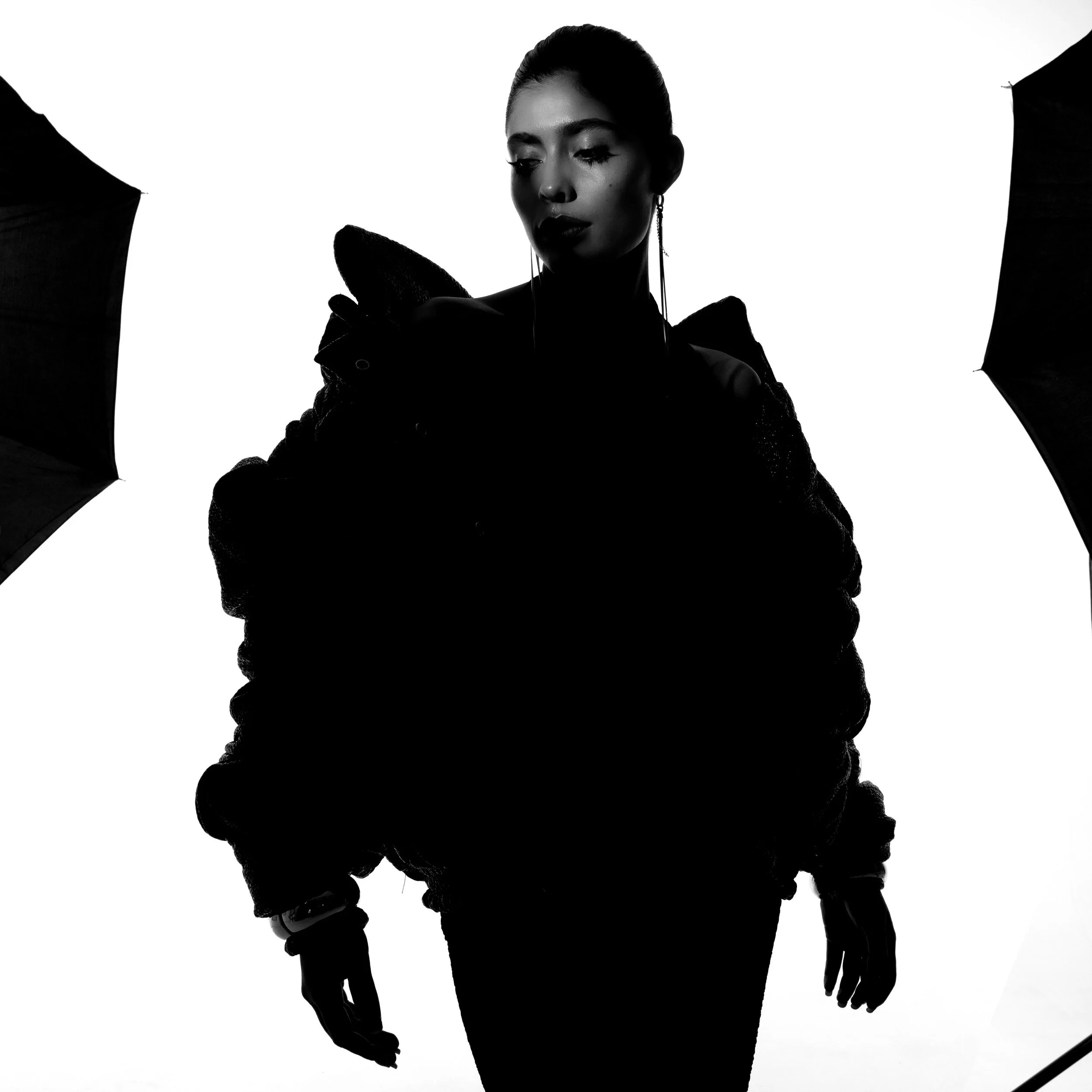 Black and white silhouette of a woman holding an umbrella, with a stark white background.