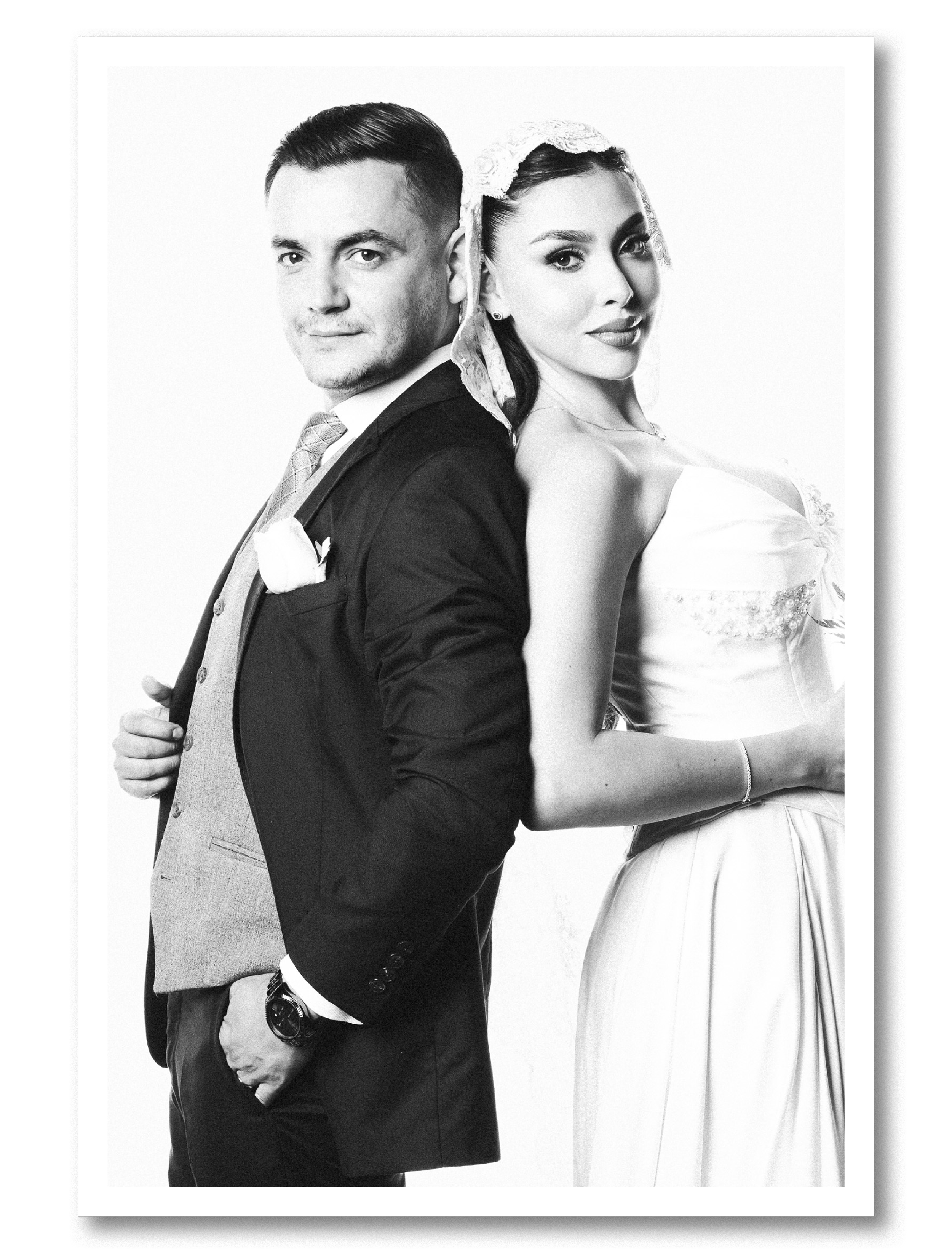 Black and white photo of a man and woman standing back to back, both dressed formally, with the man wearing a suit and the woman in a dress, facing slightly to the side.