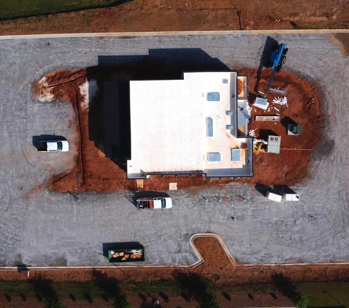An aerial view of a house under construction on a dirt lot, with construction equipment, vehicles, and building materials around the site.