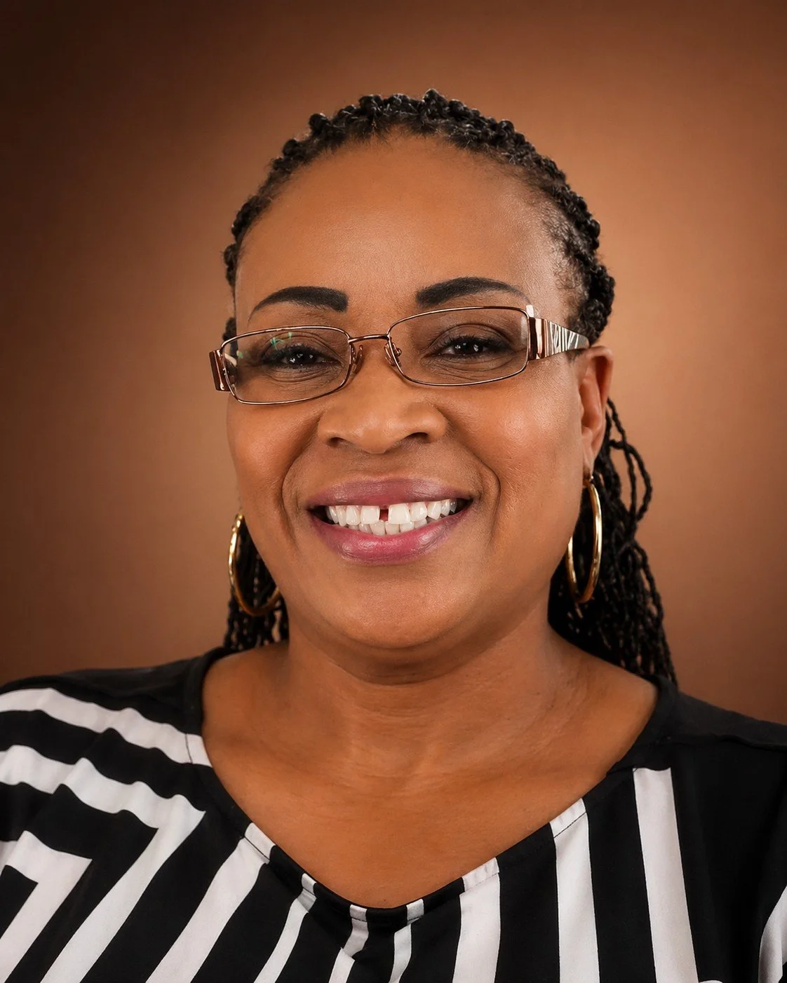 A smiling woman with glasses and earrings, wearing a black and white striped top, against a warm brown background.