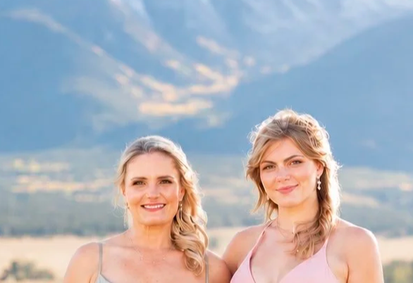 Two women with blonde hair smiling outdoors against a mountain landscape background.