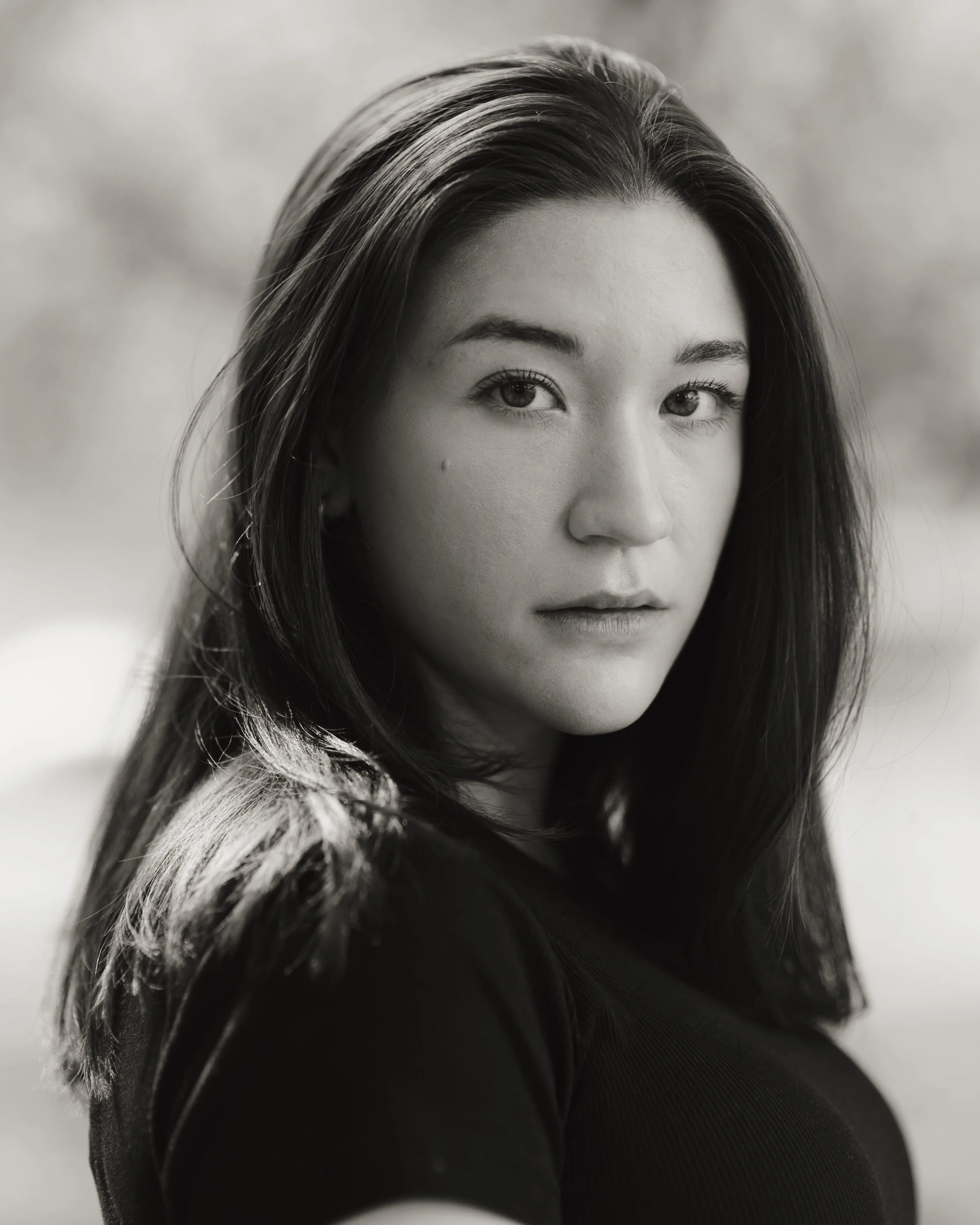 Close-up portrait of a young woman with long dark hair, light skin, and dark eyes, in black and white.