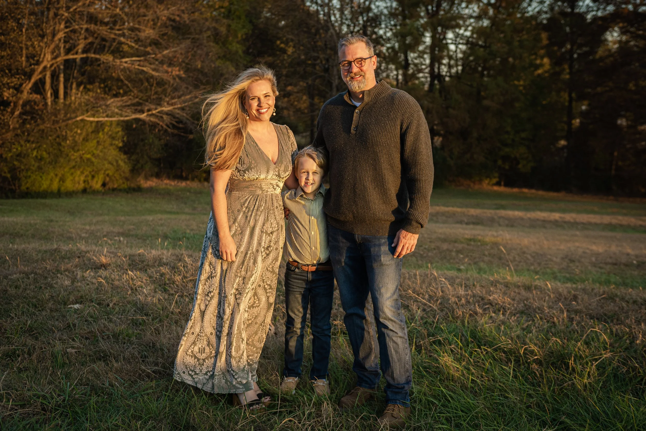 Four people, two women and two men, standing outdoors on grass during sunset in a park, smiling at the camera.