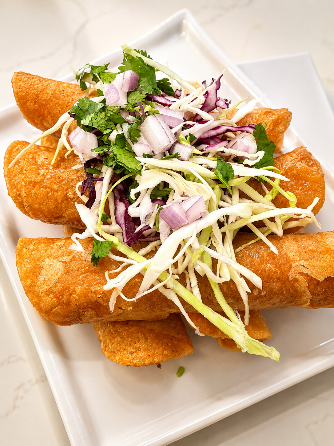 “Crispy golden rolled tacos topped with fresh cabbage slaw, red onion, and cilantro, plated for an upscale catering presentation by Highly Flavored Catering.”