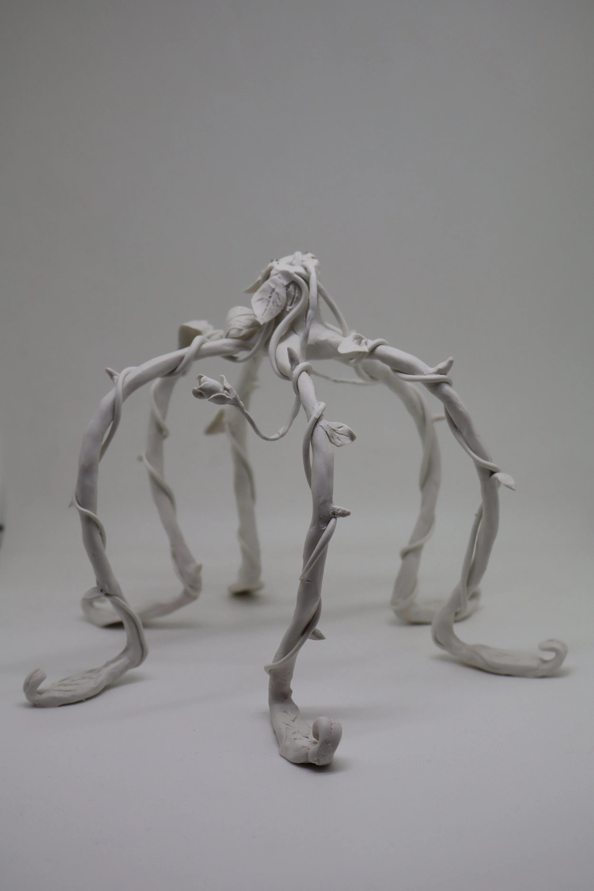 A white sculpture of a goat made from twisted wire and clay, standing on a plain white background.