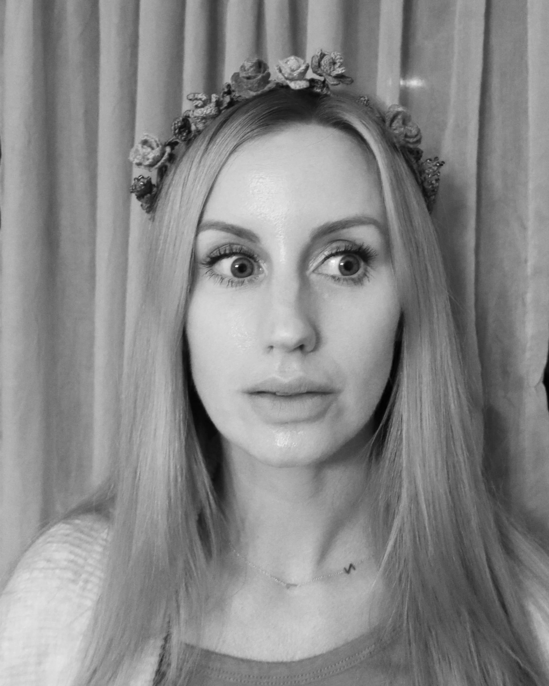 Black and white photo of a woman with long straight hair, wearing a floral headband, and a T-shirt with a small letter 'W' tattooed on her chest.