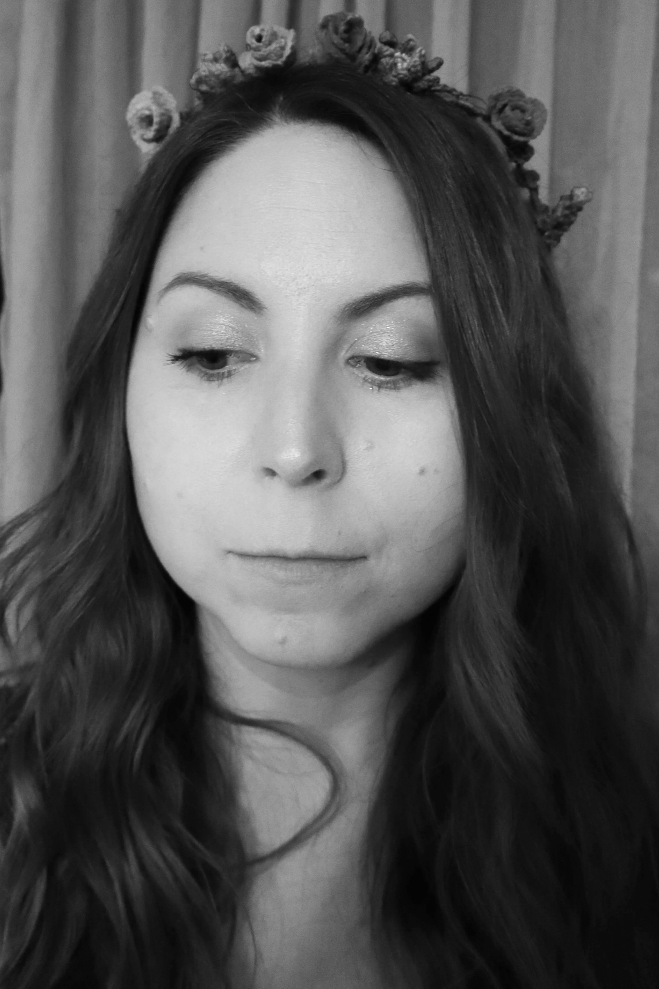 Close-up black-and-white photo of a woman with long wavy hair, wearing a floral headband, with her eyes partially closed.