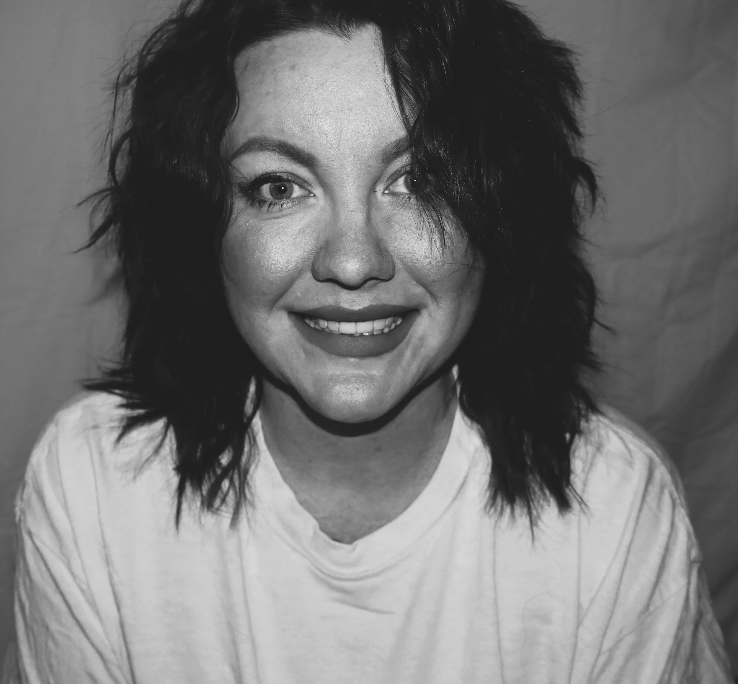 Close-up of a woman's face, smiling, with dark, curly hair, in black and white.