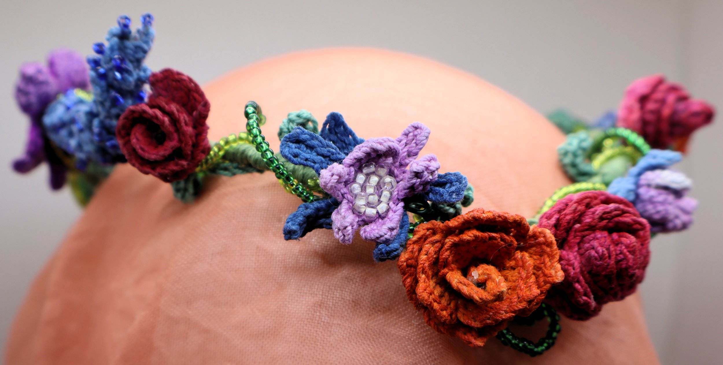Colorful handmade crochet flowers and beads form a floral headband or crown worn on a person's head.