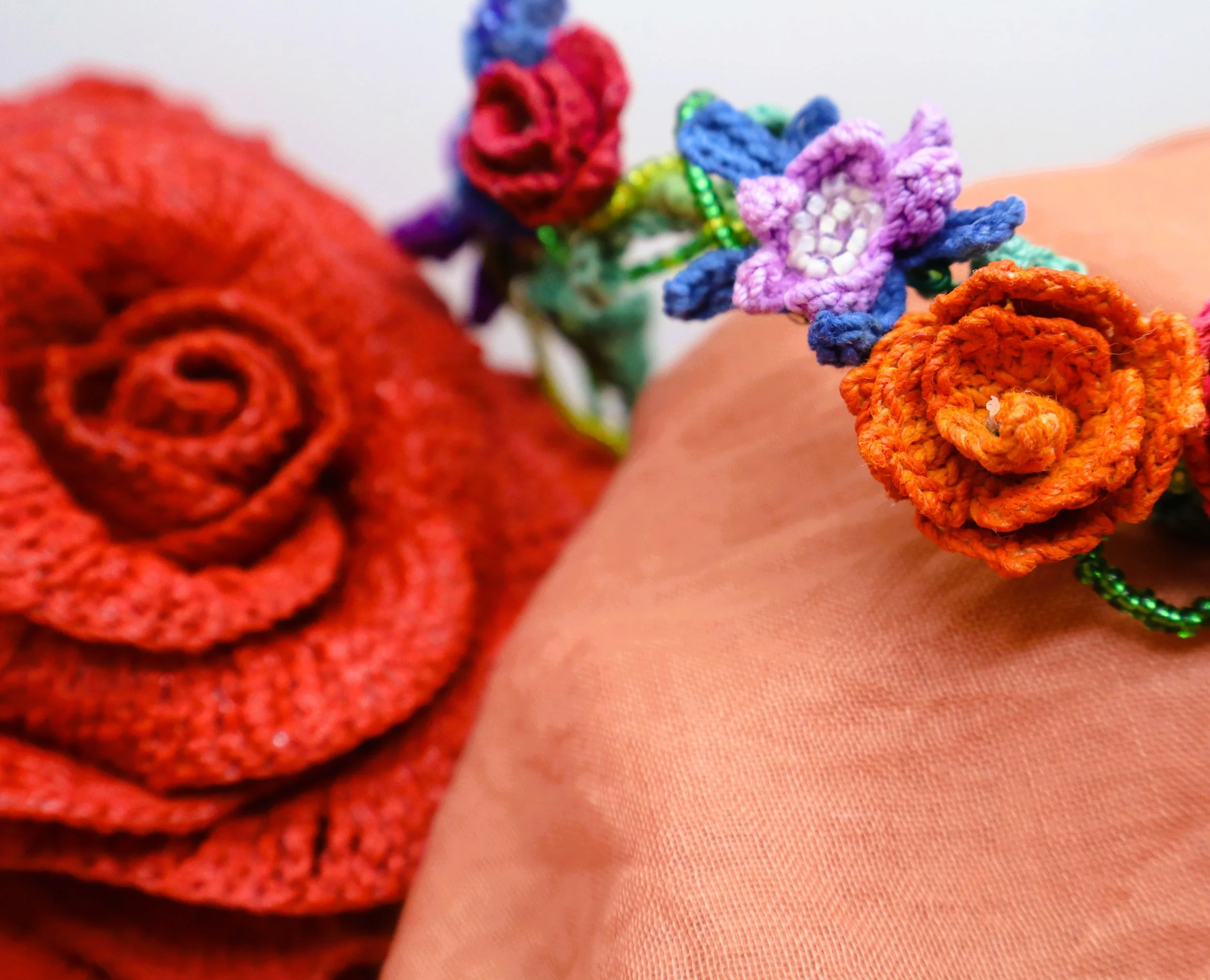 Close-up of colorful crochet flowers with beads on a pink fabric background.