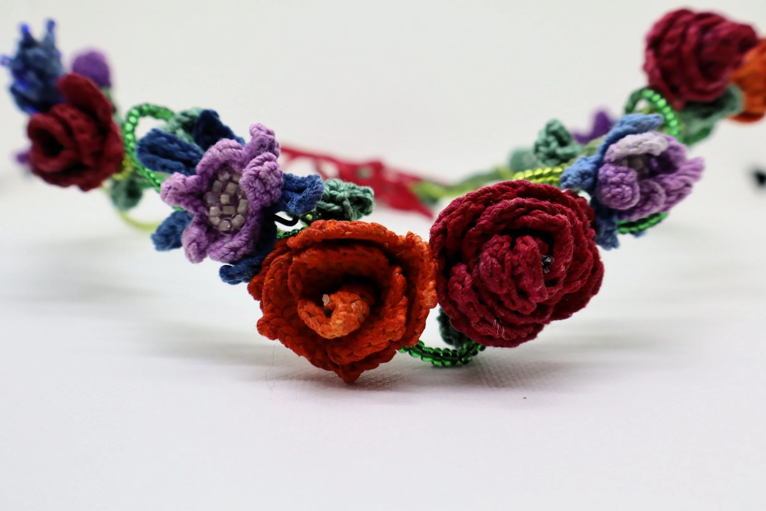 Colorful handmade crochet flower bracelet featuring red, purple, blue, and orange flowers with green stems and beaded accents on a plain white background.
