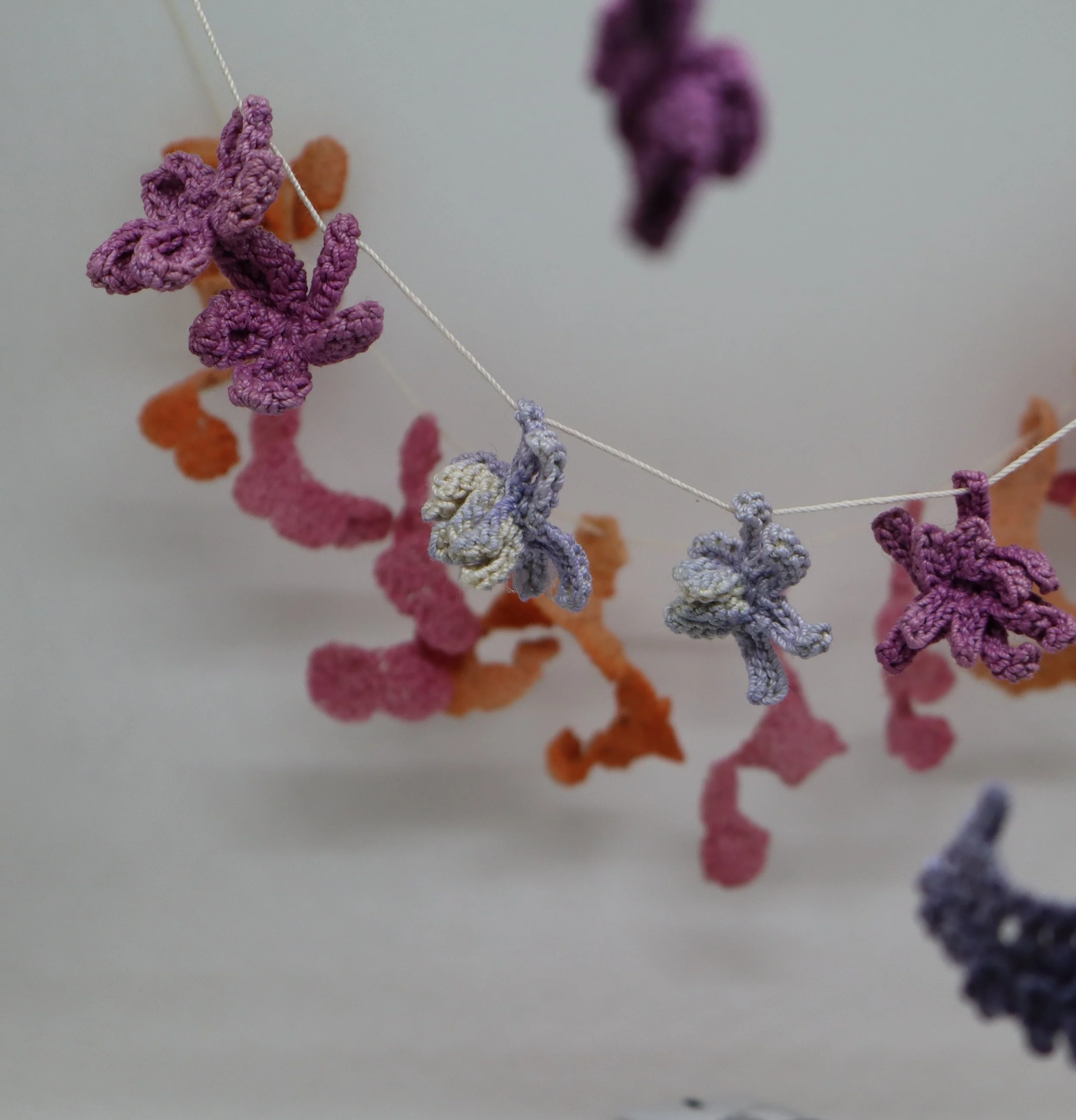 Close-up of colorful knitted or crocheted butterfly and animal-shaped decorations hanging on a string against a plain background.