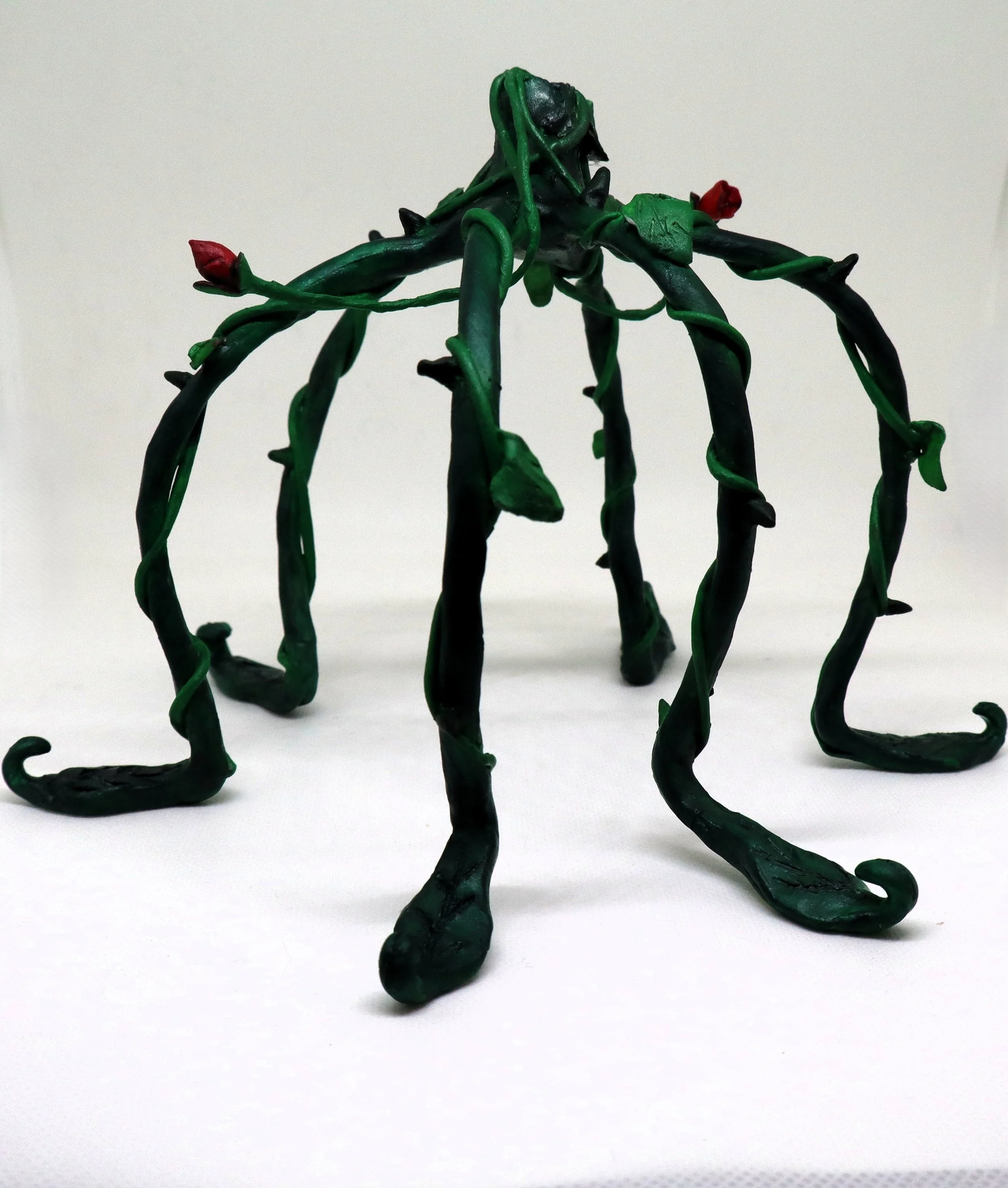 A sculpture made of intertwined green and black wires with red accents, resembling a spider or insect.
