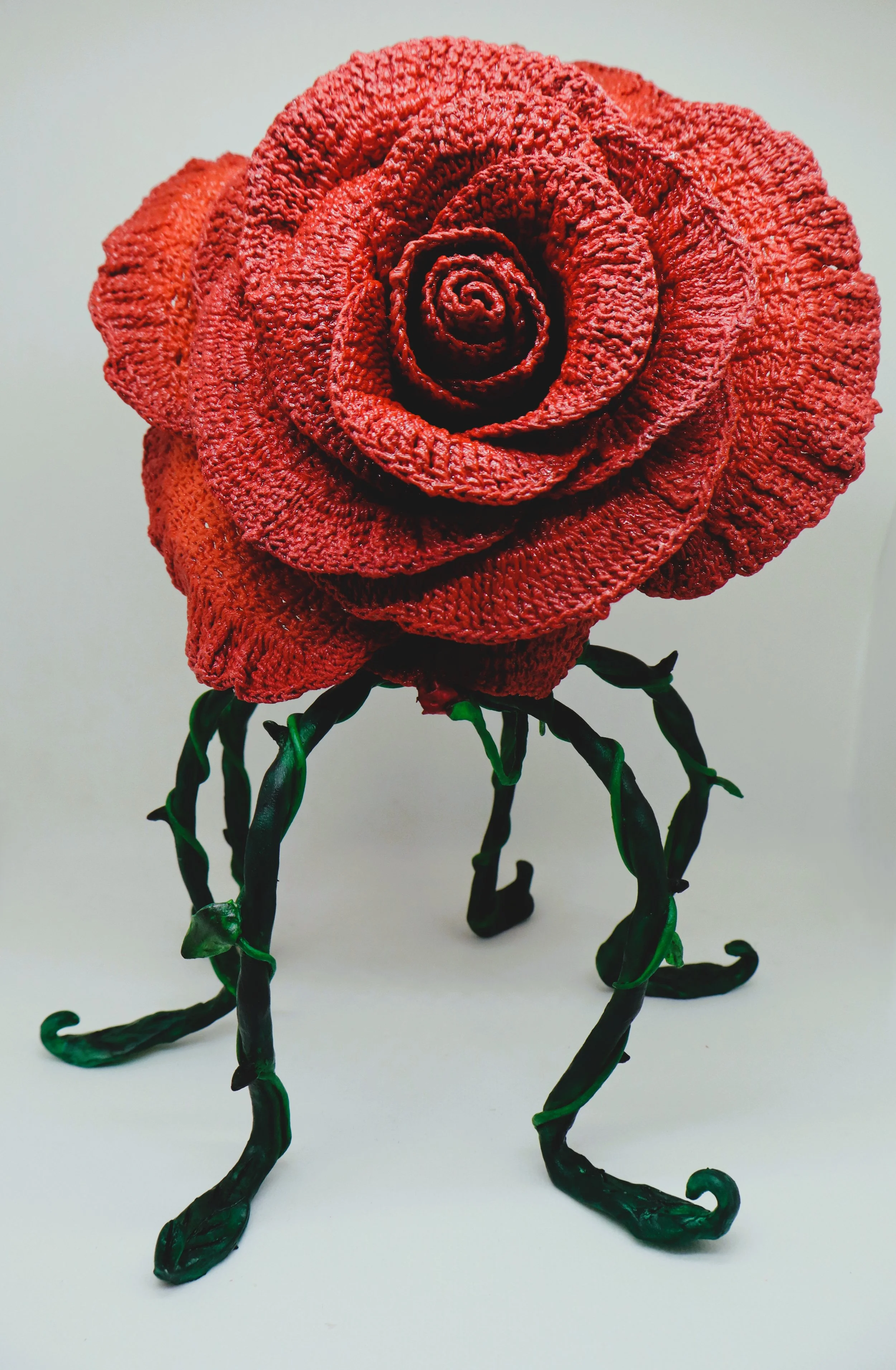 A sculpture of a red rose with black, twisted stem and leaves made of metal or similar material.