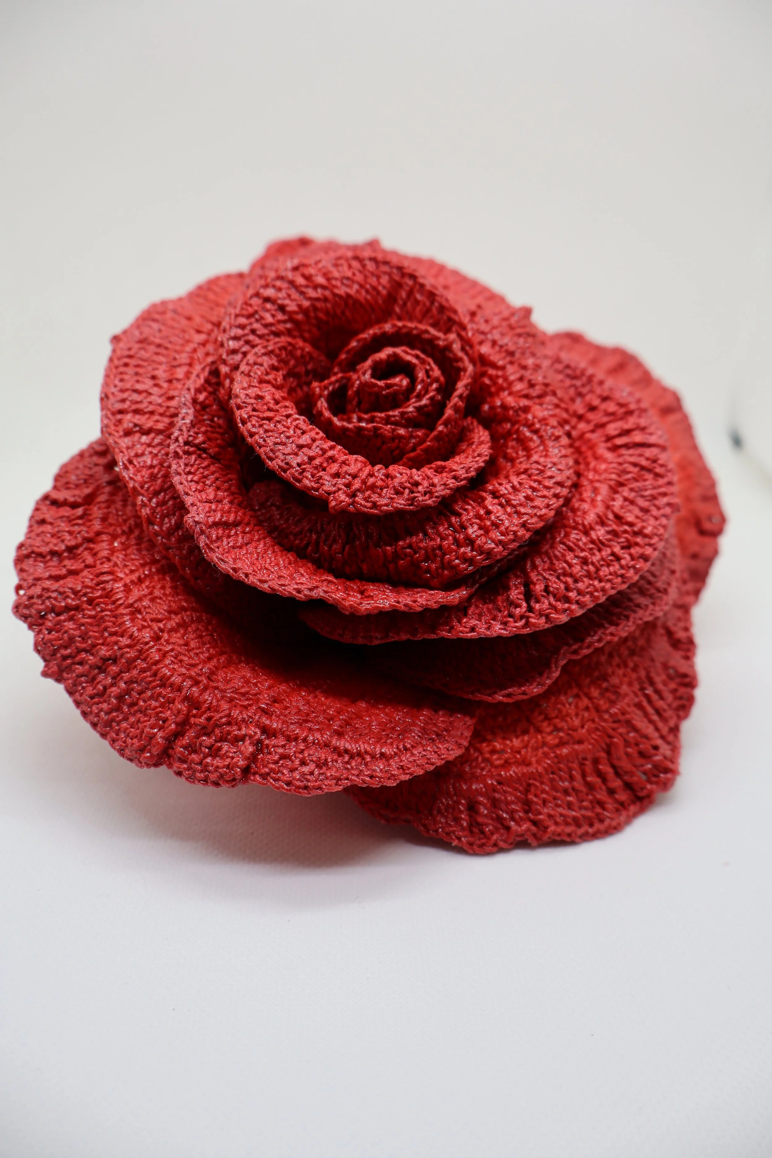 Red towel folded to resemble a rose with layered petals on a white background.