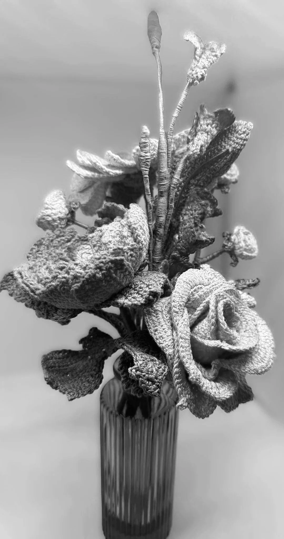 Close-up black-and-white photograph of a withered, dried flower bouquet in a glass vase against a blurred background.