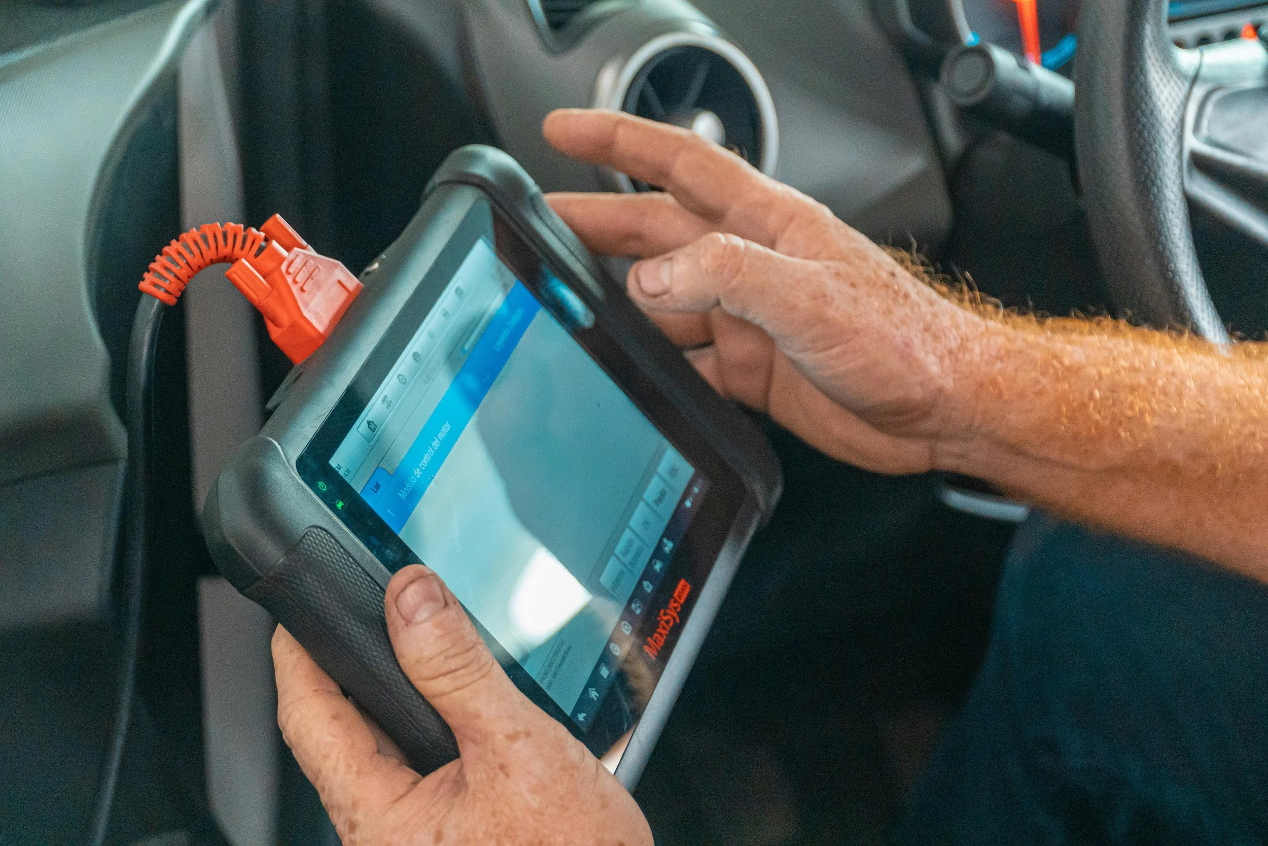 An elderly person's hand holding a mobile device with a screen displaying a message, inside a vehicle with a dashboard and air vents visible.