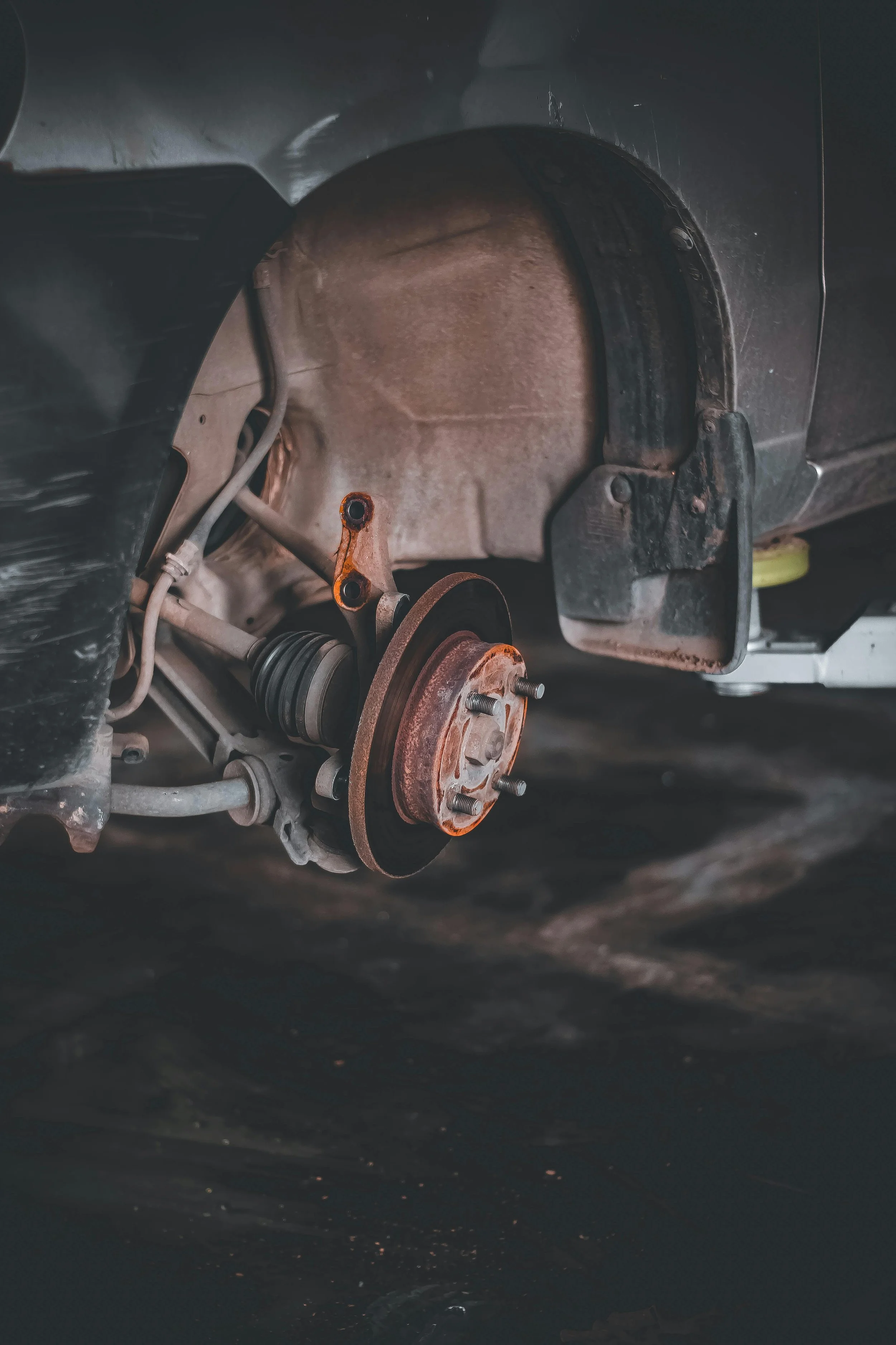 Close-up of a car's wheel hub and suspension components with the wheel removed, showing the brake disc, rust on the hub, and suspension parts.