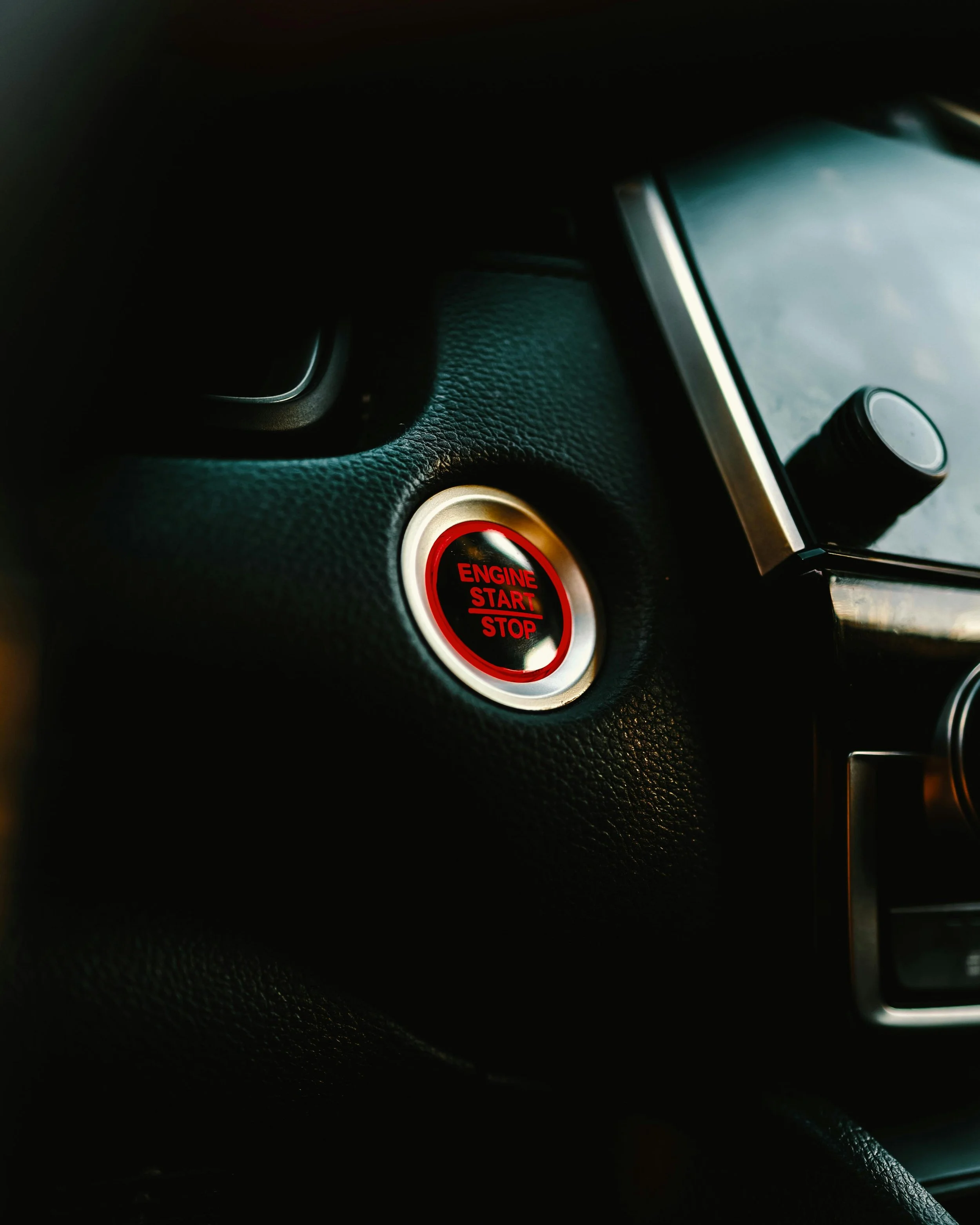 Close-up of a car's interior showing a red and black engine start button on a textured dashboard.