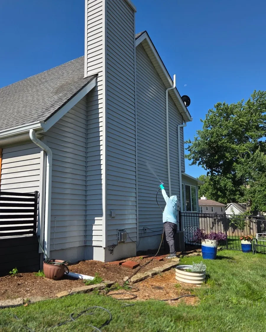 Steve Johnson, owner of CurbSprout LLC, applying professional-grade soft washing solution to the upper siding and eaves of a Johnson County home from ground level