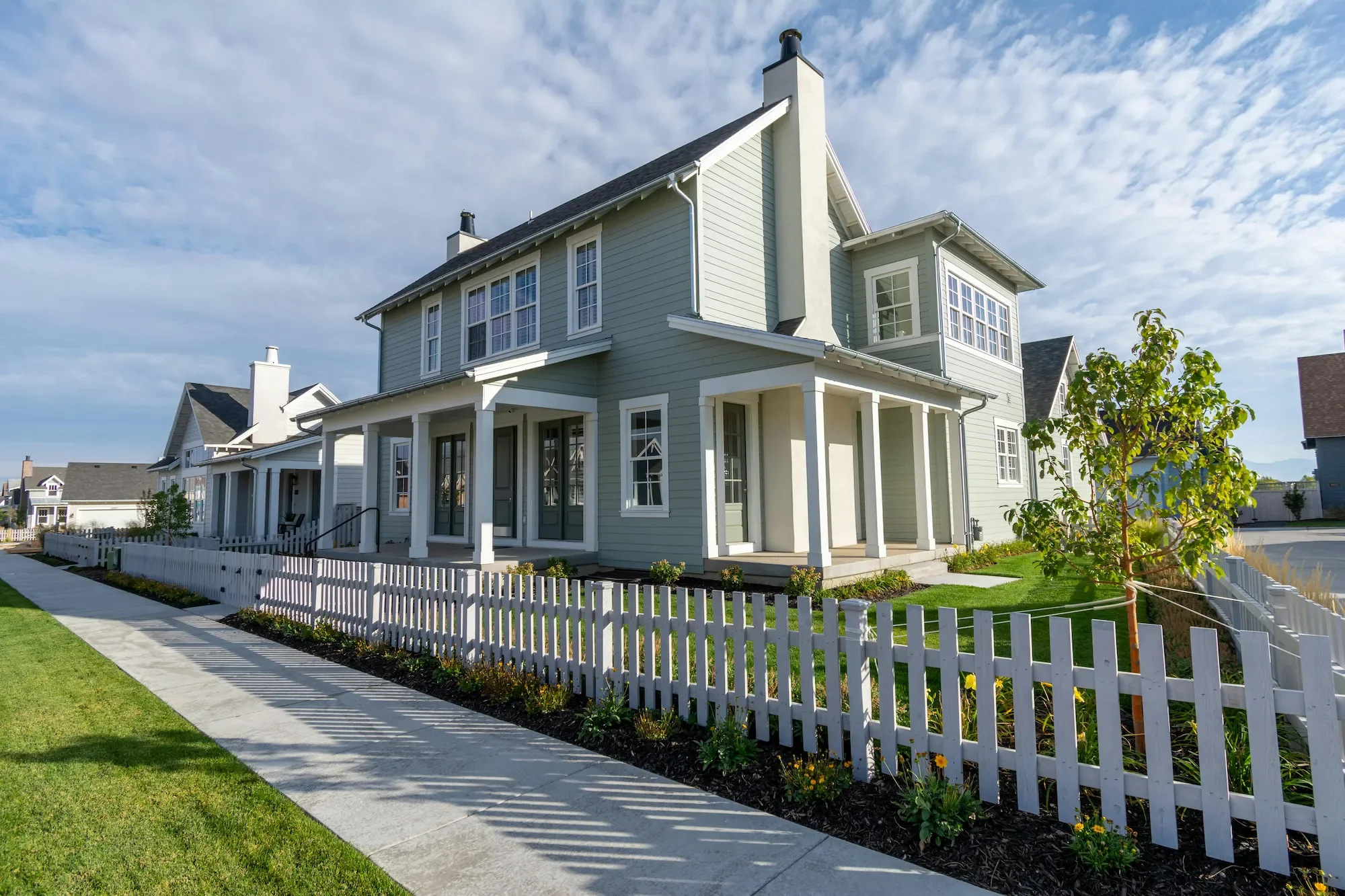 Grey two-story home with white picket fence — fence washing removes algae and weathering from wood and vinyl fencing