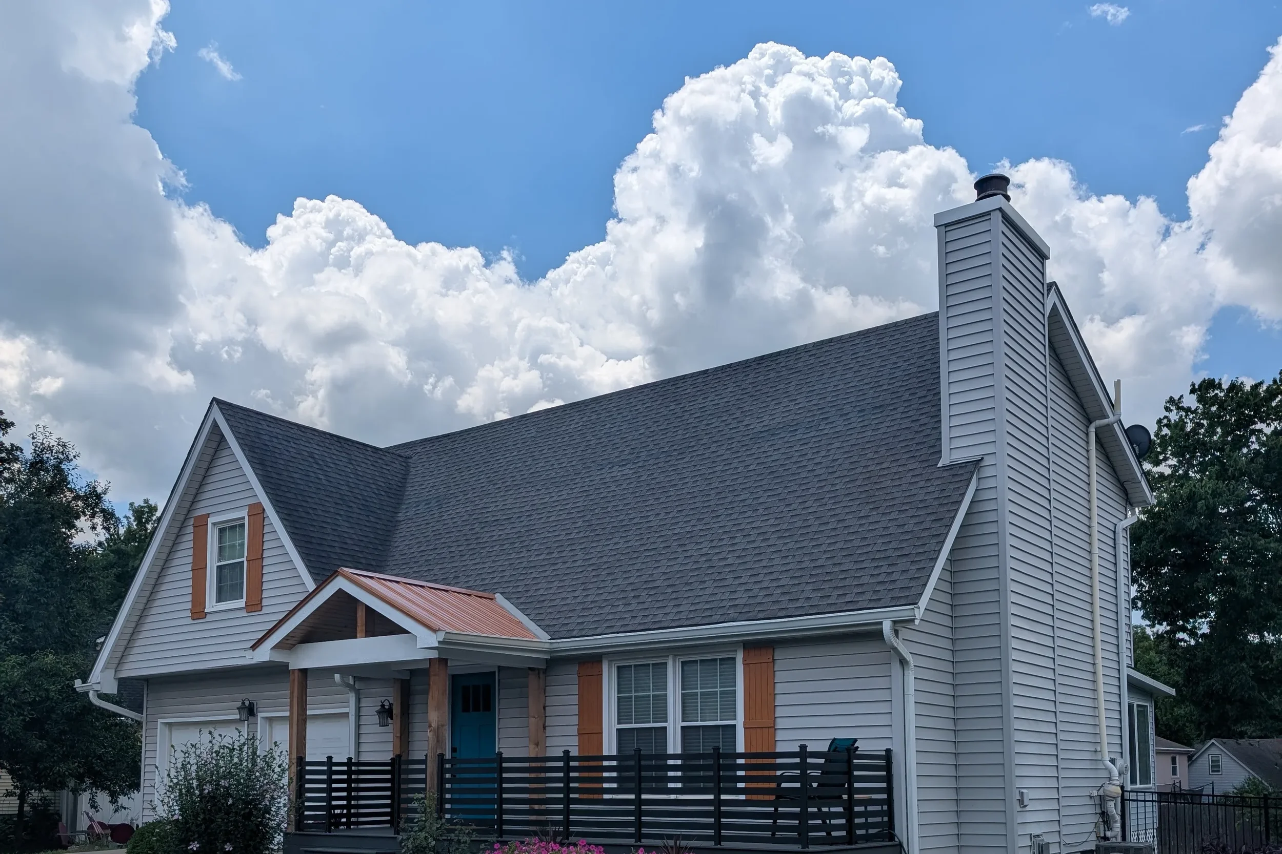 Soft washed home exterior in Johnson County KS — clean gray vinyl siding, copper roof accent, and teal front door after professional house washing by CurbSprout