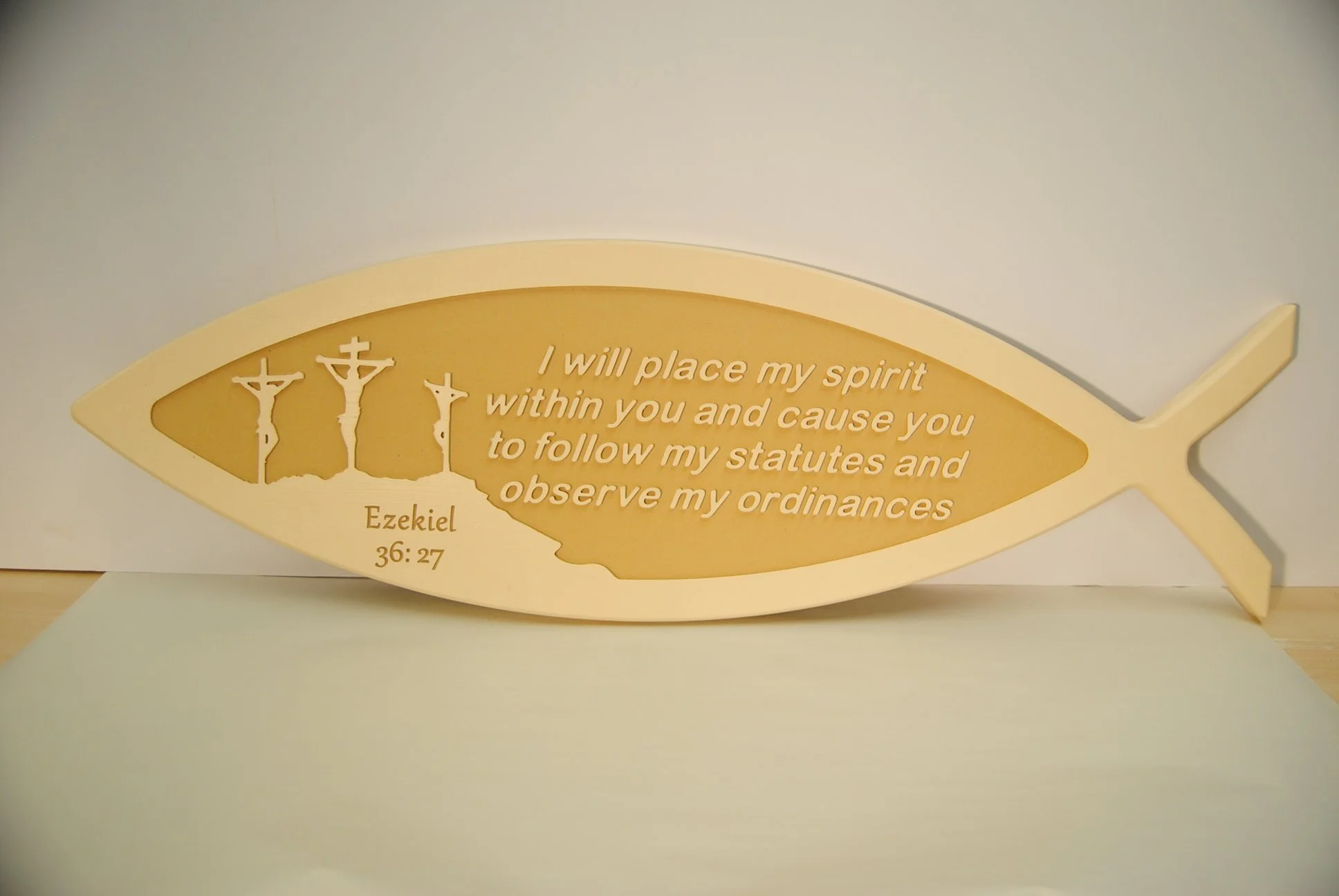 A fish-shaped plaque with the text: 'I will place my spirit within you and cause you to follow my statutes and observe my ordinances.' Ezekiel 36:27, along with three crucifixions images.