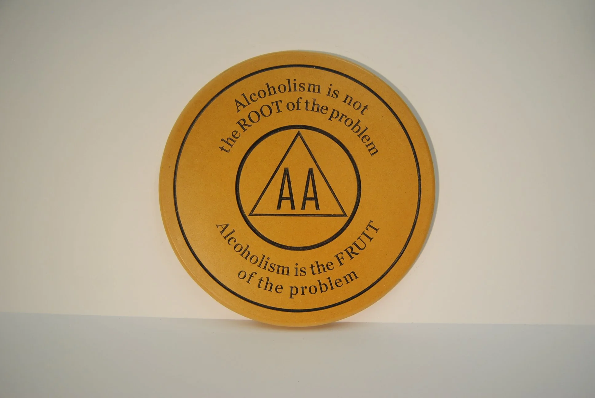 A circular sign with the AA (Alcoholics Anonymous) logo and the text, "Alcoholism is the ROOT of the problem. Alcoholism is the FRUIT of the problem."
