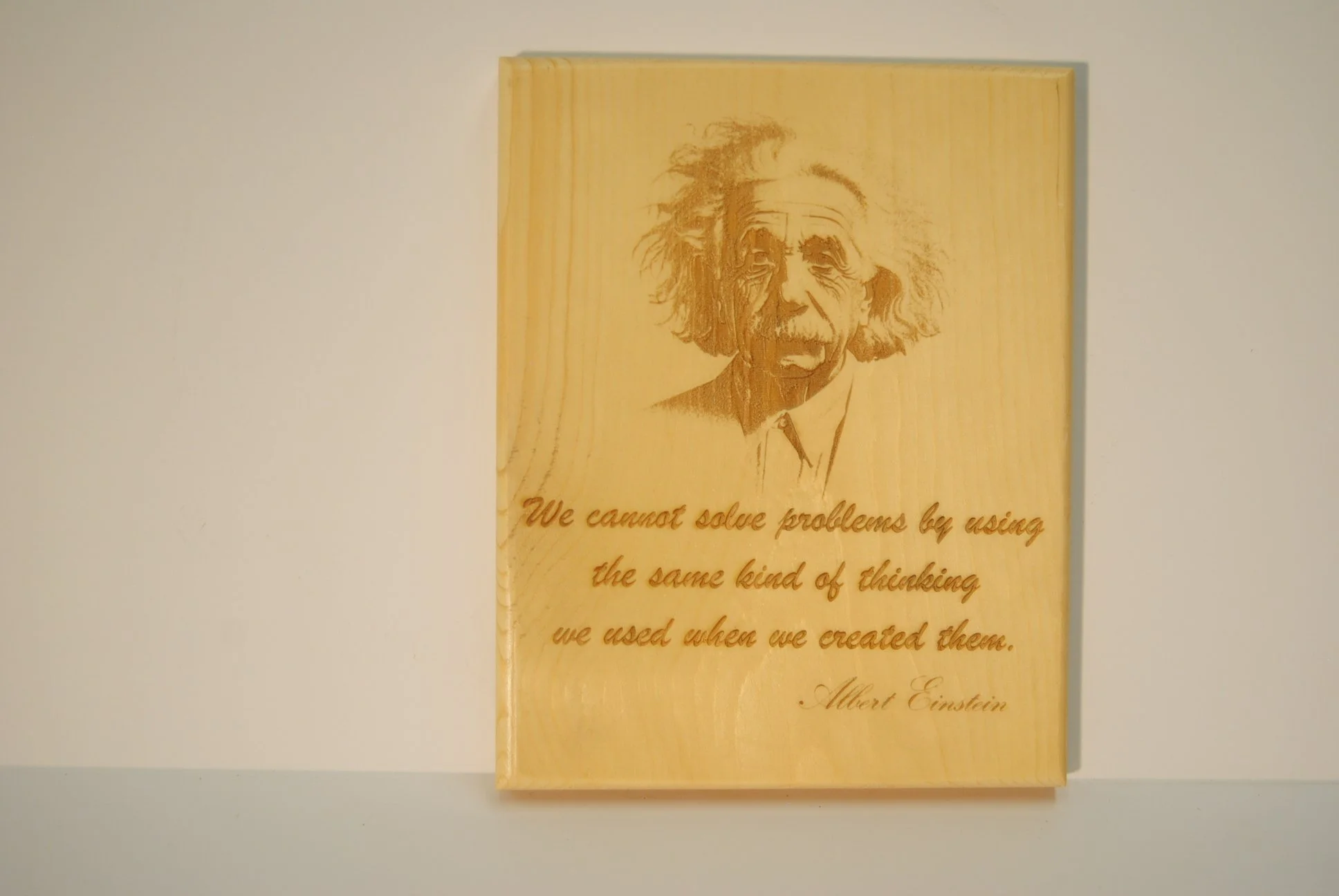 A wooden plaque with an engraved portrait of Albert Einstein, accompanied by his quote: "We cannot solve problems by using the same kind of thinking we used when we created them."