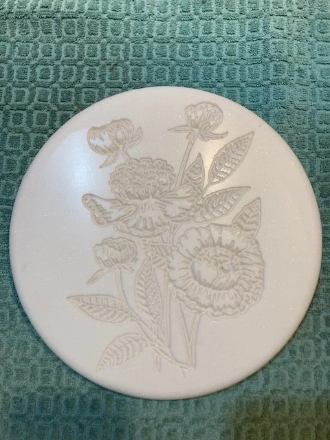 A round white plate with a floral engraved design, placed on a textured teal tablecloth.