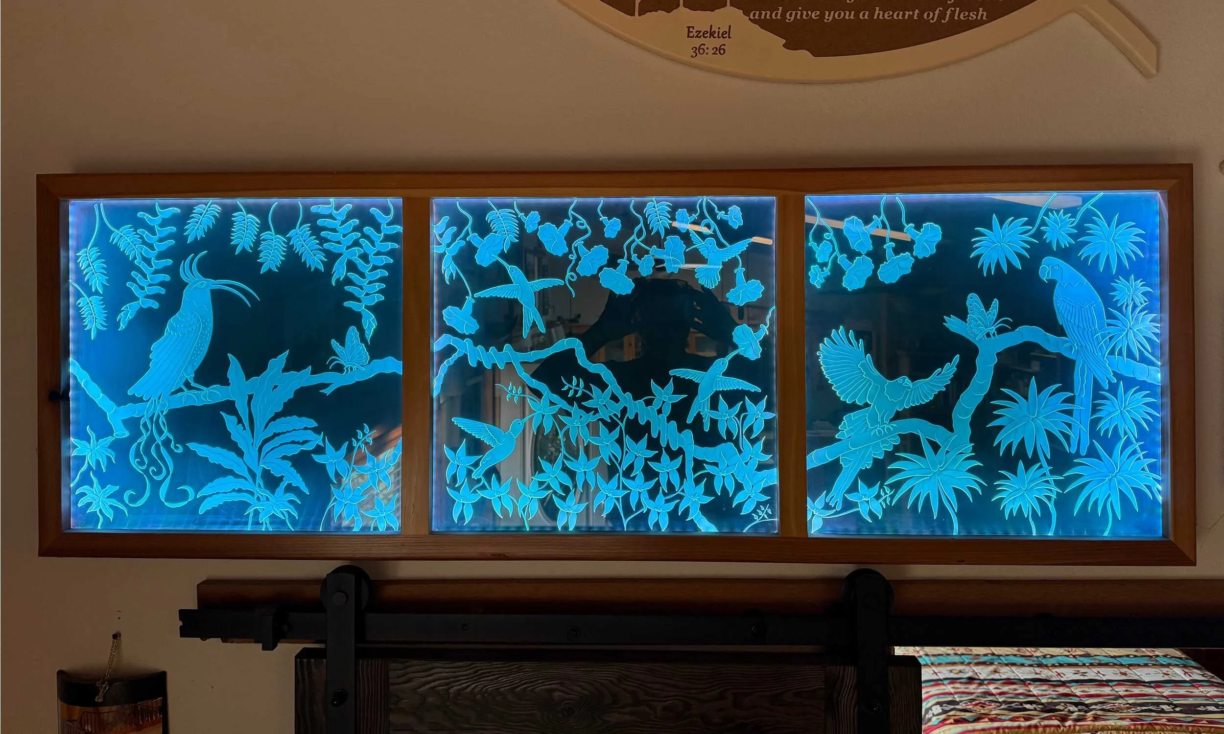 Decorative backlit panel featuring silhouettes of various tropical plants, hummingbirds, and parrots in blue neon outline, framed in wood.