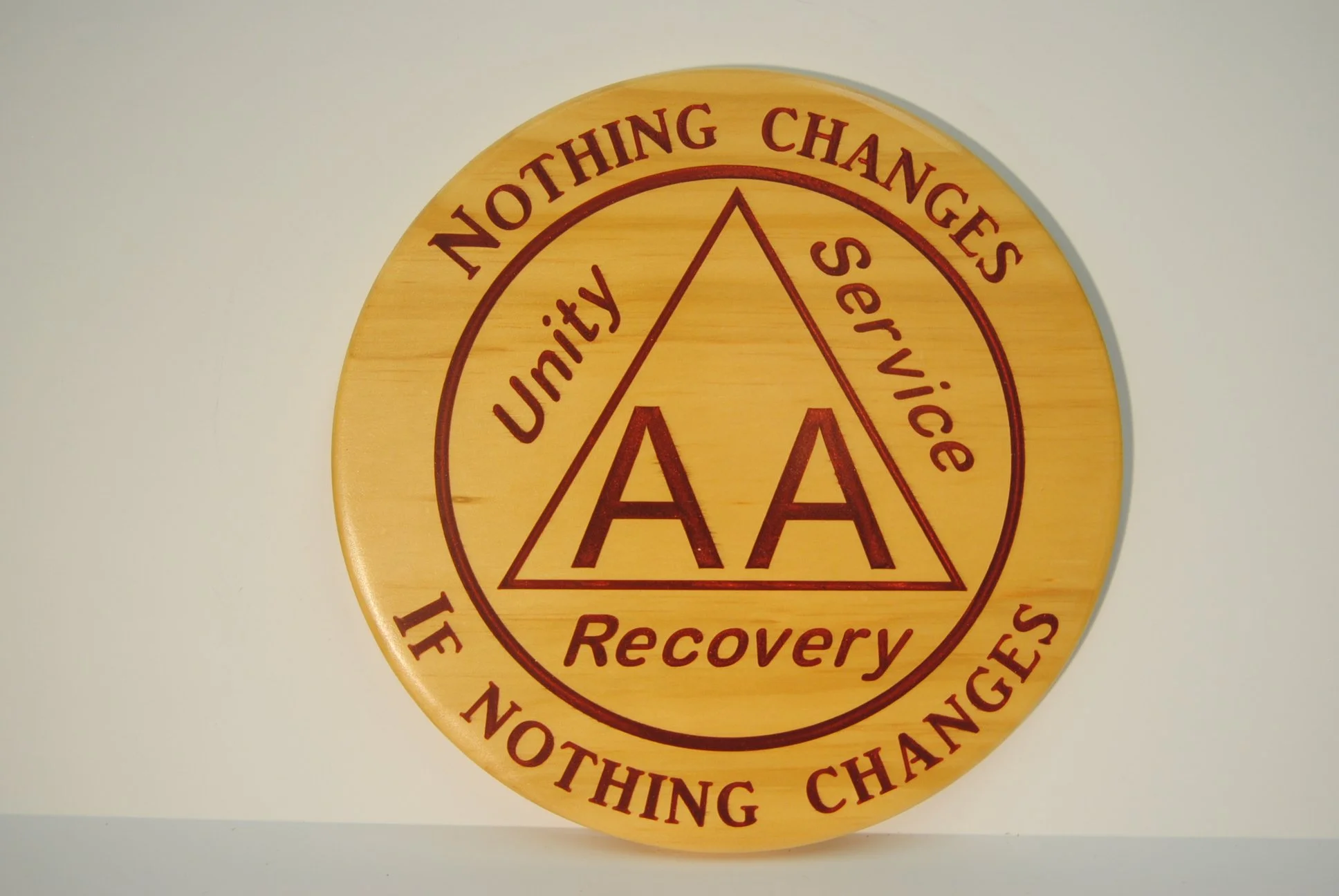 Circular wooden plaque with the words 'Nothing Changes Until Something Changes' and 'Recovery' engraved around a central triangle with 'Unity', 'Service', and 'Personal Responsibility' inside it, and 