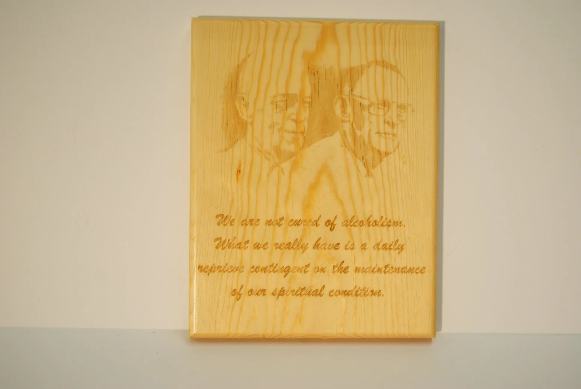 Wooden plaque with engraved sketch of three elderly men and a quote about alcohol and spiritual condition.