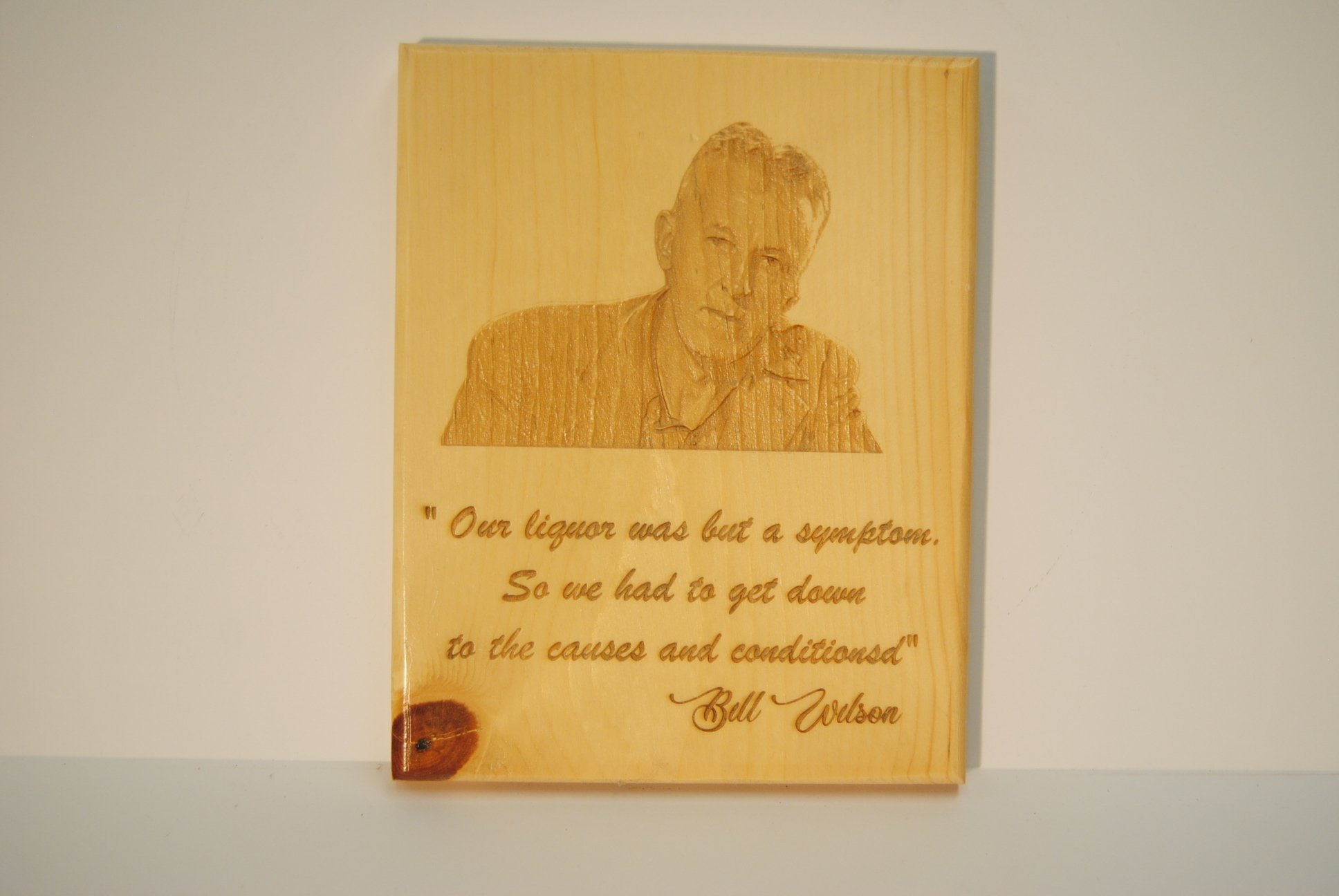 Wooden plaque with an engraved image of a man and a quote that reads, 'Our liquor was but a symptom. So we had to get down to the causes and conditions' - Bill Wilson.