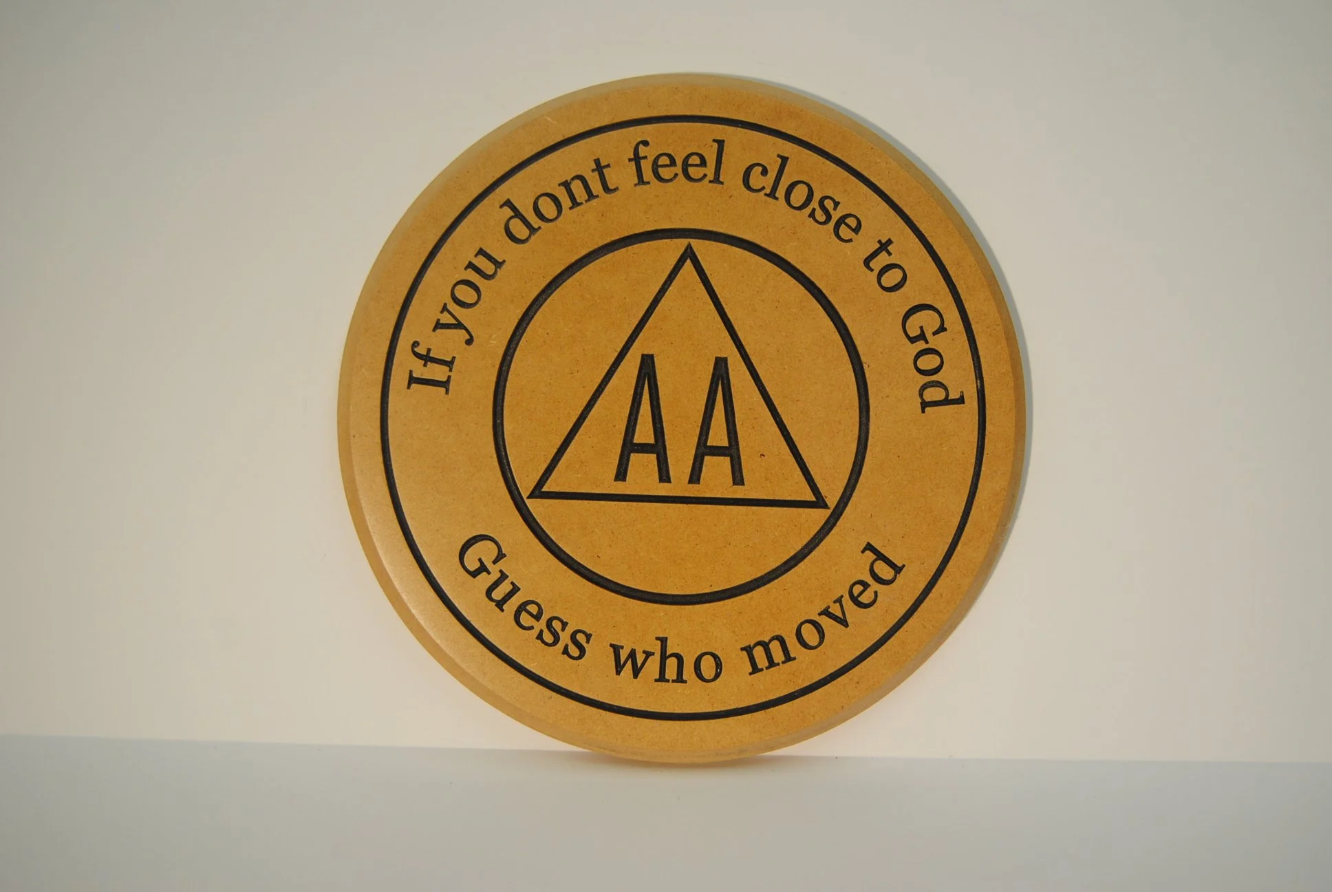 Circular wooden plaque with black text and the AAA logo. The text reads: "If you don't feel close to God, guess who moved."