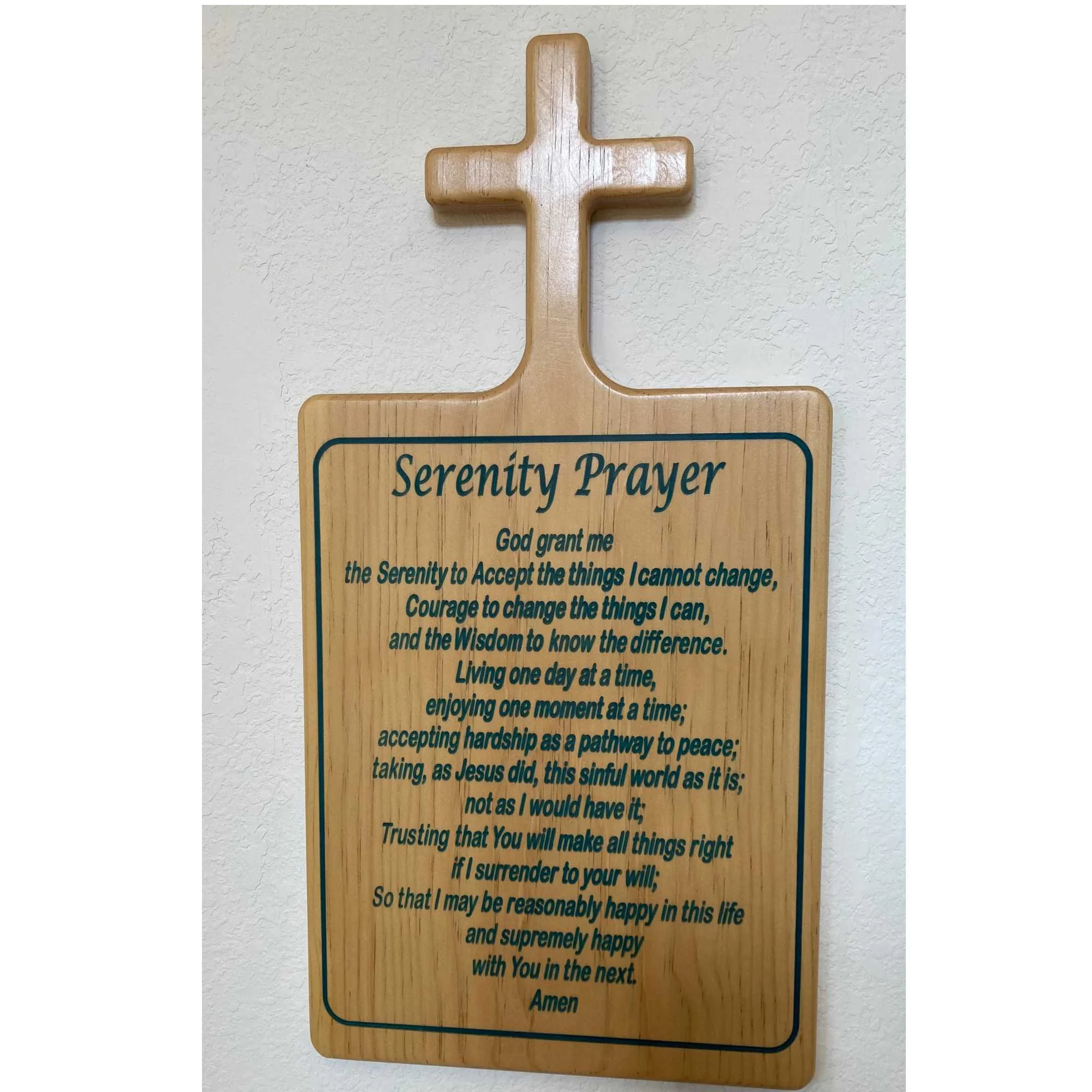 Wooden cross-shaped sign with a Serenity Prayer written on it, attached to a textured white wall.