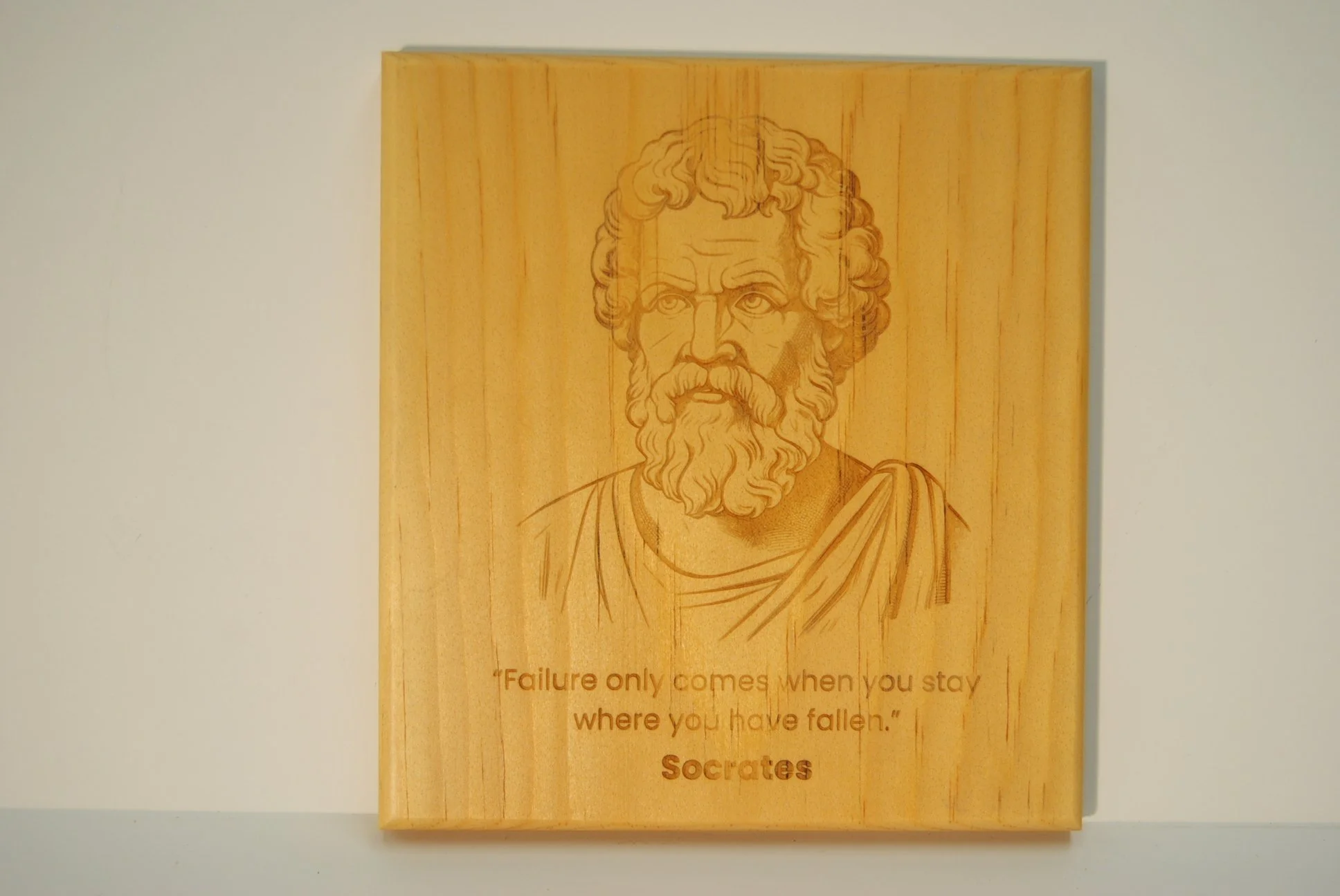 Wooden plaque with a line drawing of Socrates' face and a quote that reads 'Failure only comes when you stay where you have fallen.'