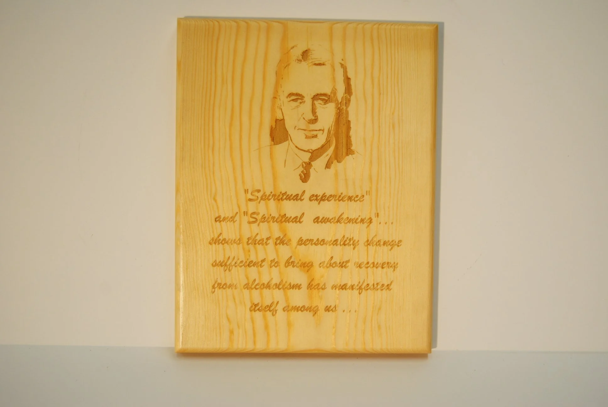 A wooden plaque with a carved portrait of a man and an engraved quote about spiritual awakening and recovery from alcoholism.