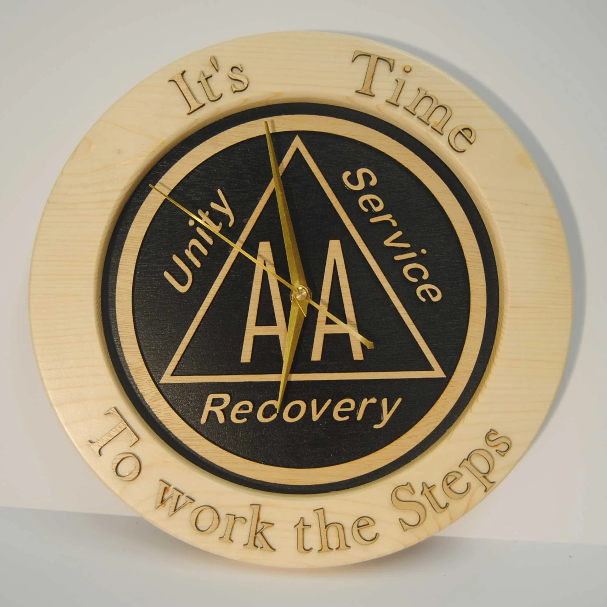 A round wooden wall clock with black and gold accents, inscribed with motivational phrases such as "It's Time," "Recovery," and parts of other words, featuring gold clock hands.